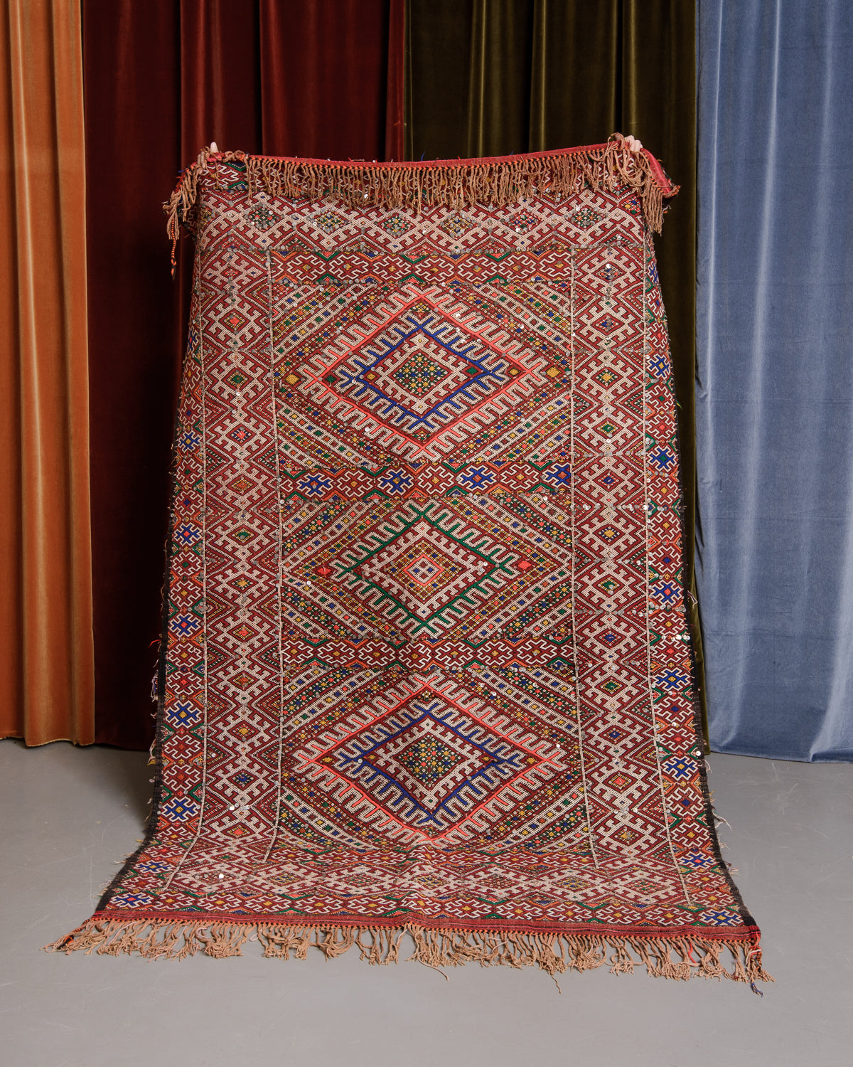 Detailed Vintage Kelim being held in front of velvet curtains. 