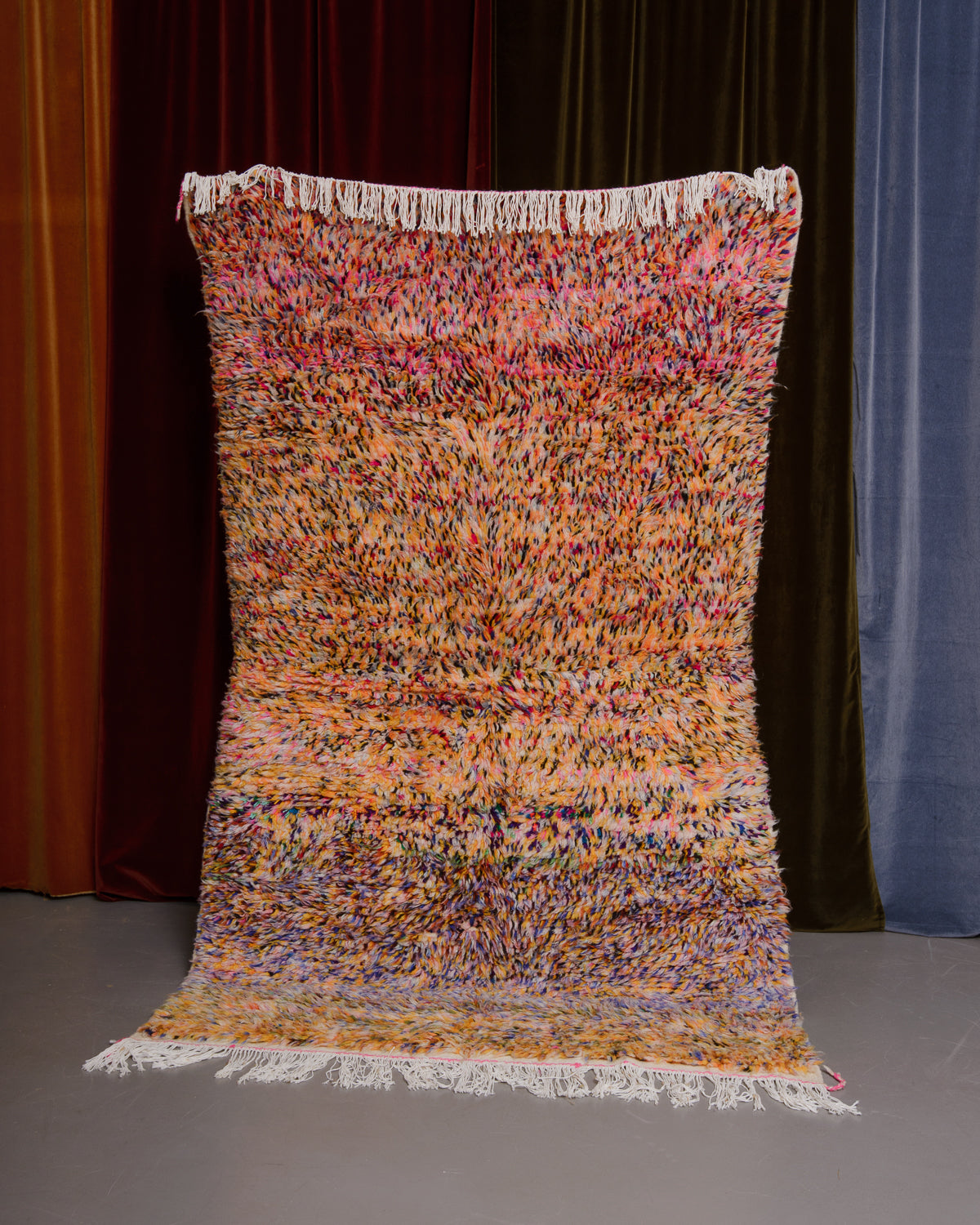 Azilal rug held in front of velvet curtains. 