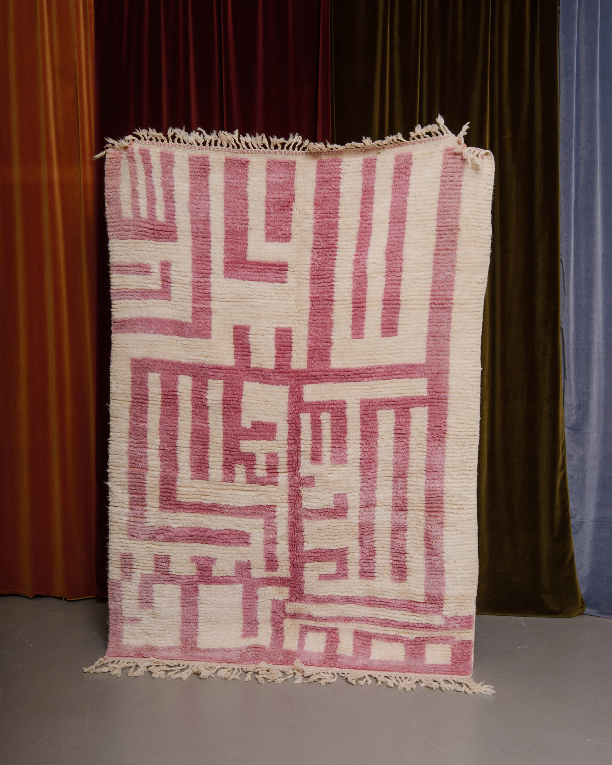 Azilal rug held in front of velvet curtains. 