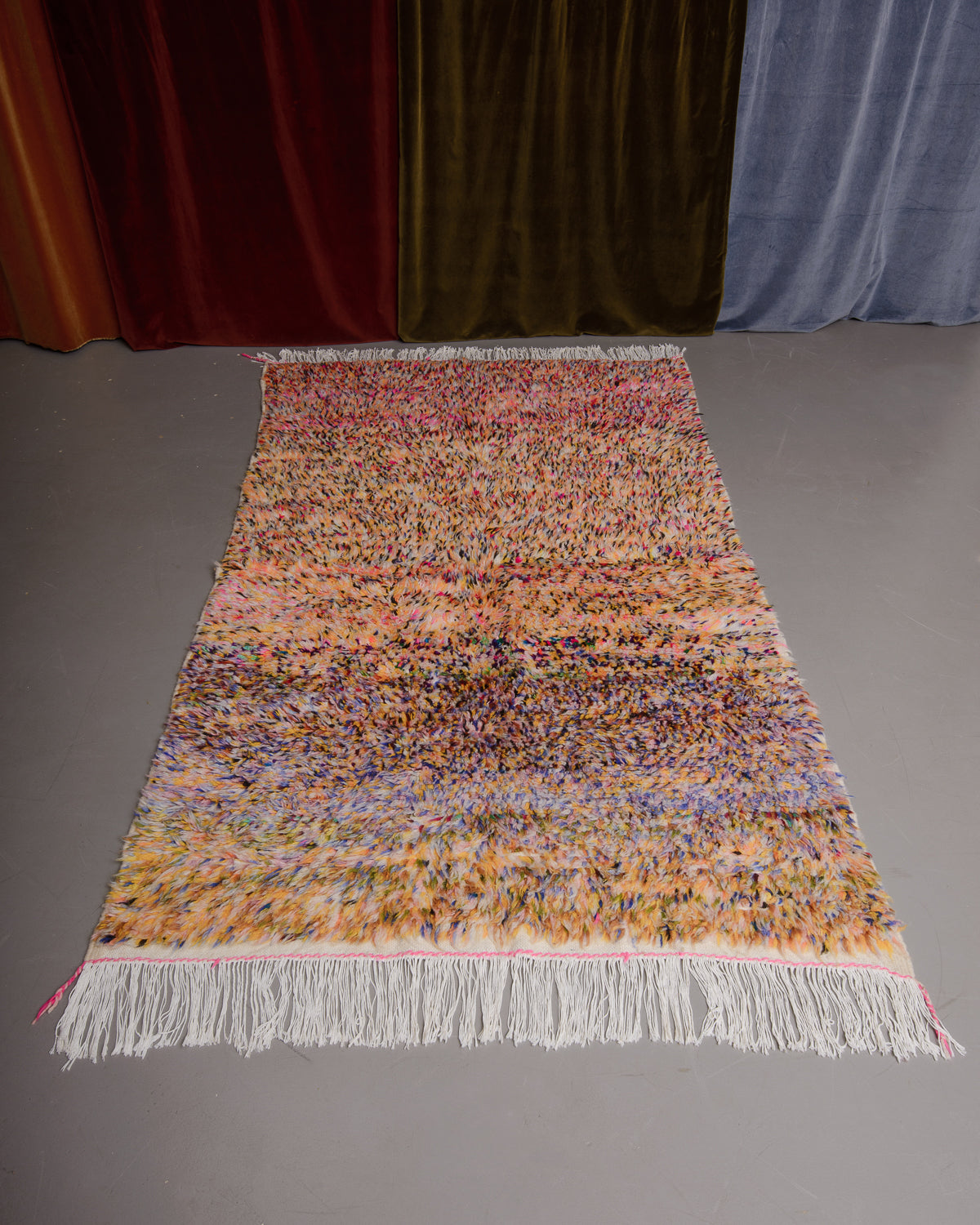 Azilal rug featuring colourful design on a grey floor in front of curtains.