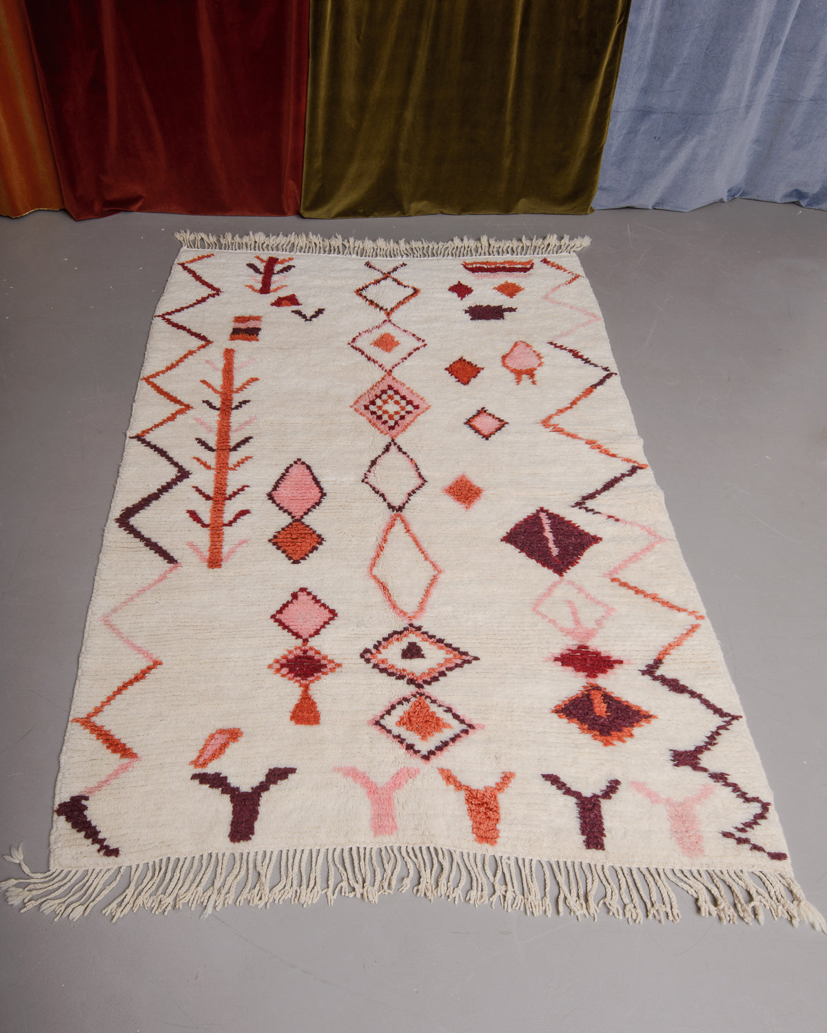 Azilal rug featuring colourful design on a grey floor in front of curtains.