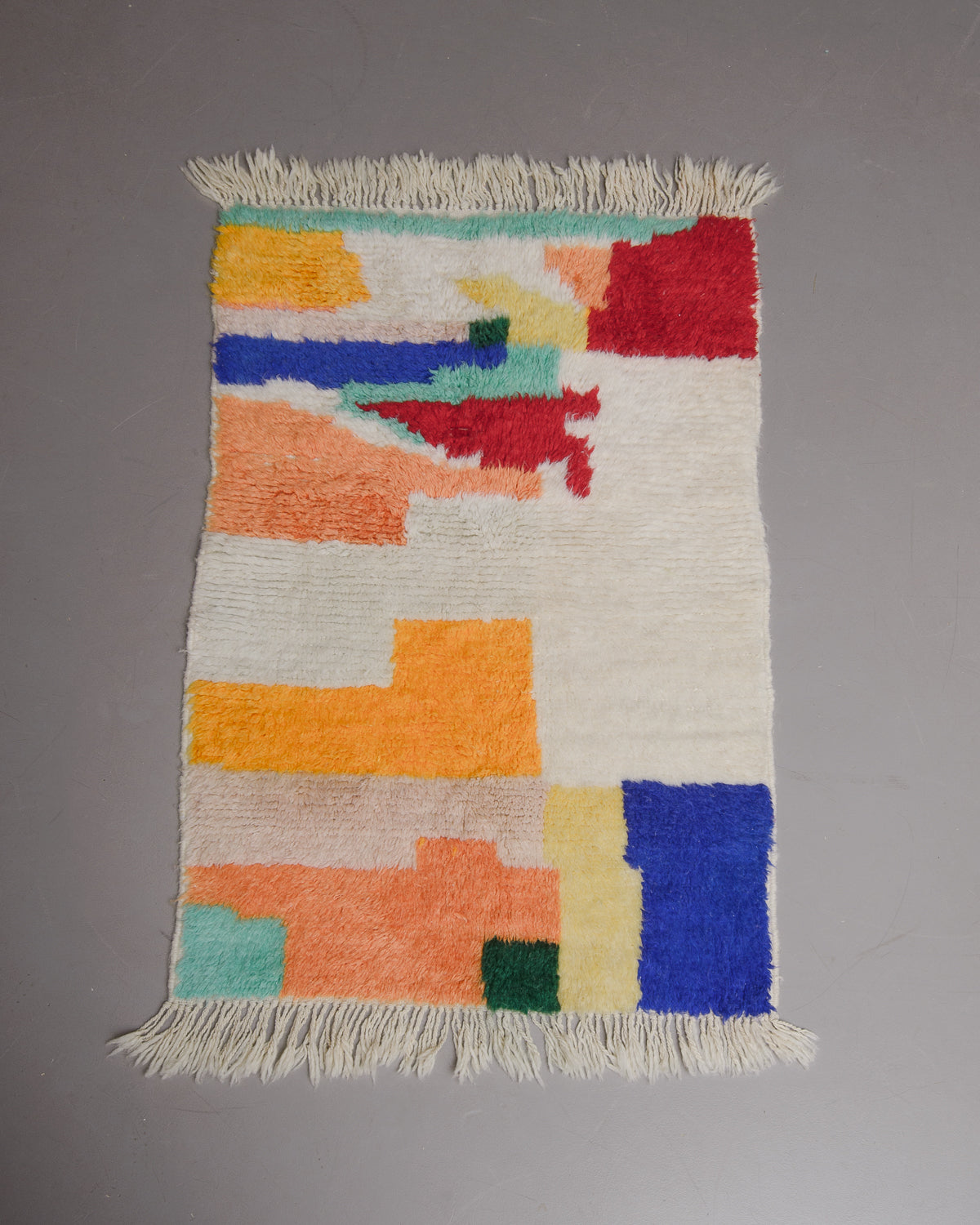 Small azilal rug with bright colours and soft, brushed sheep's wool on grey floor.