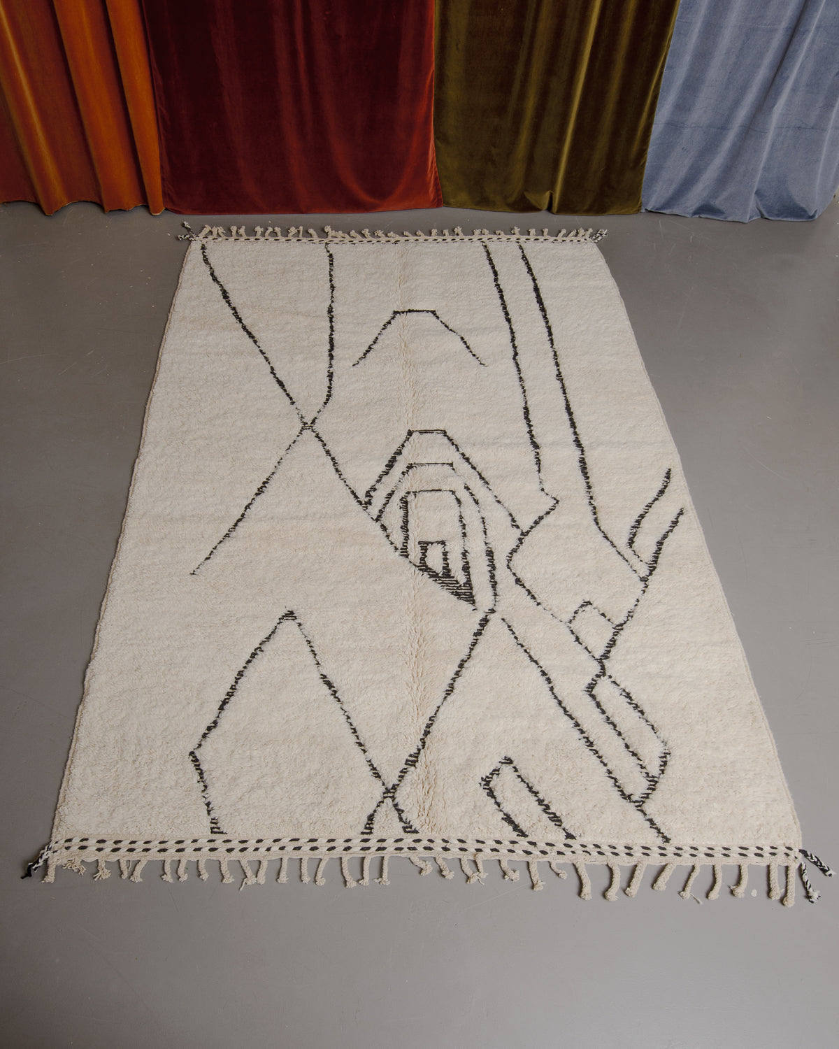 Berberlin Beniourain rug on grey floor in front of velvet curtains.