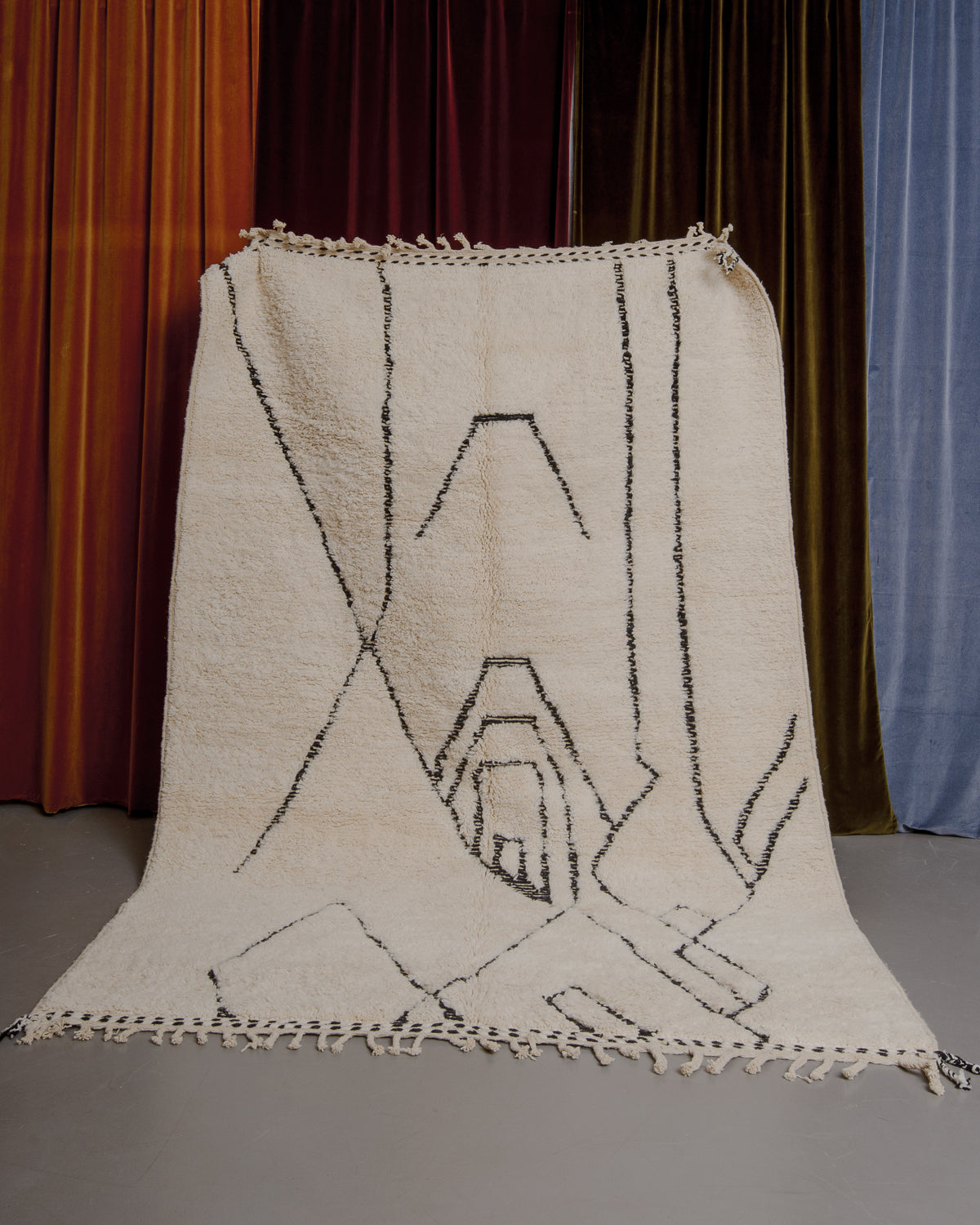 Cream and black Berberlin Beniourain rug held up in front of velvet curtains.