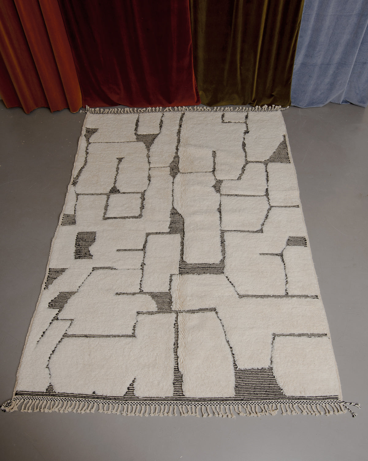 Berberlin Beniourain rug on grey floor in front of velvet curtains.