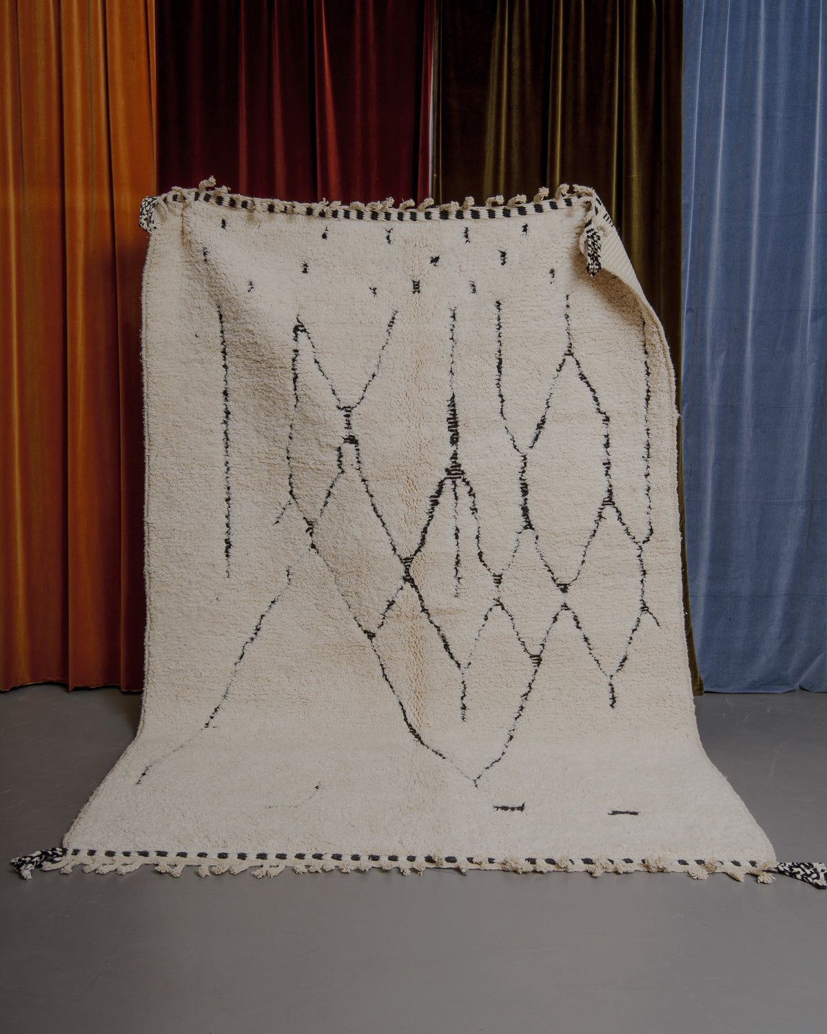 Berberlin Beniourain rug held in front of velvet curtains. 