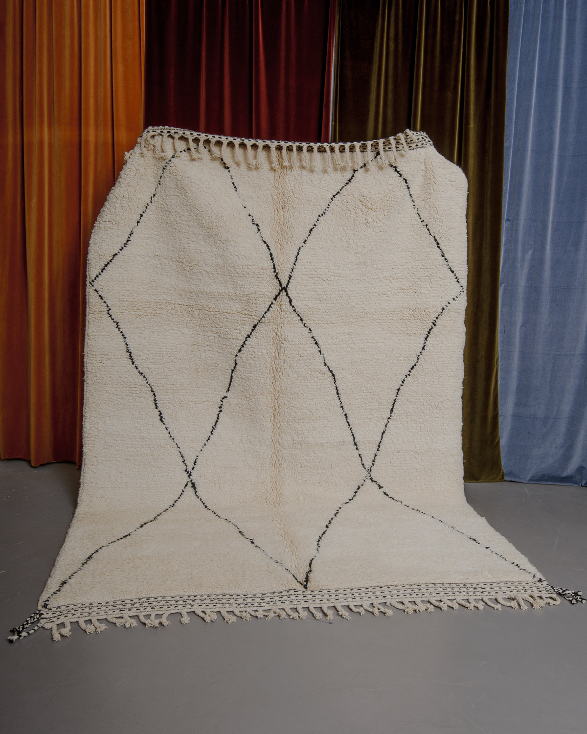 Cream and black Berberlin Beniourain rug held up in front of velvet curtains.