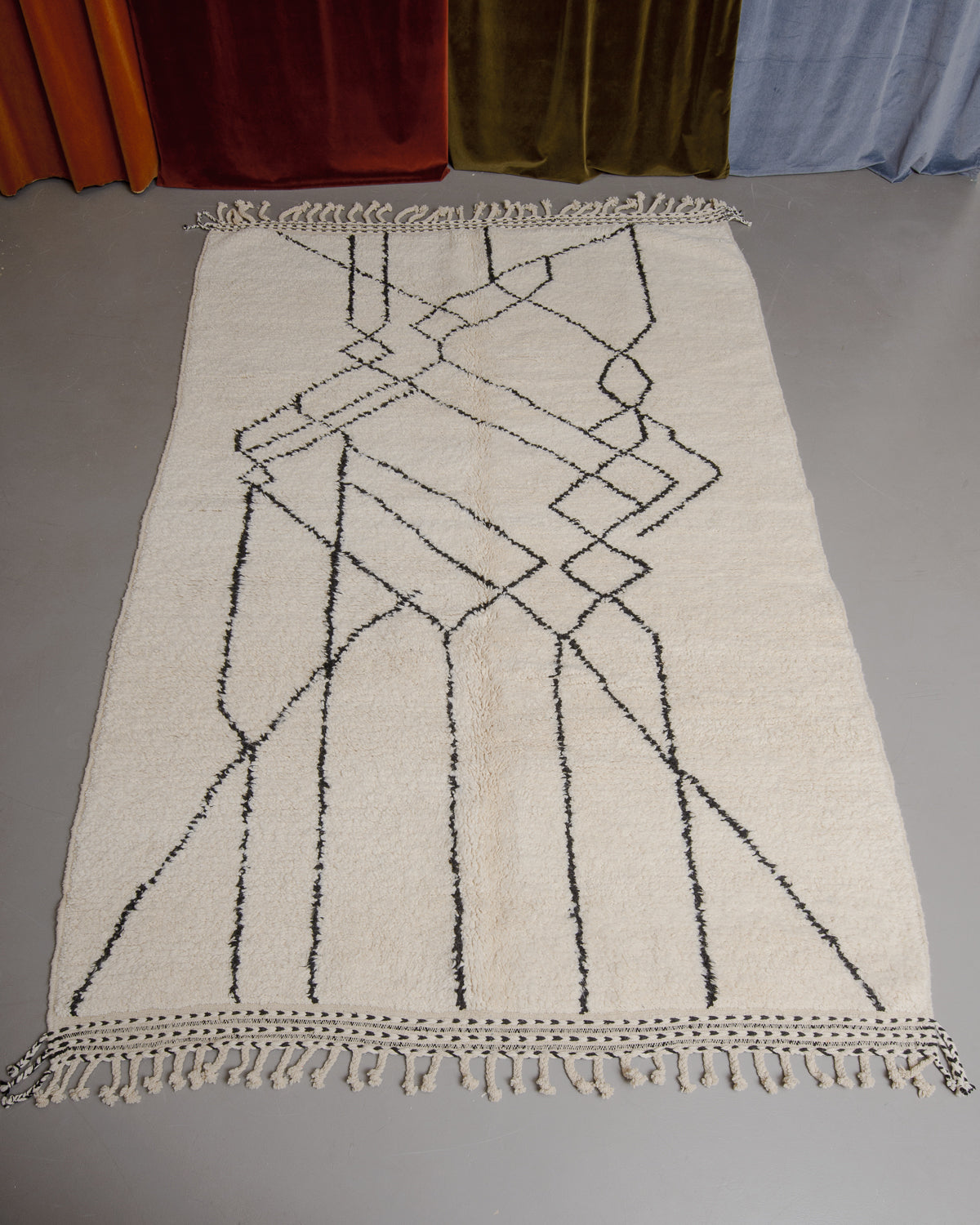Berberlin Beniourain rug on grey floor in front of velvet curtains.