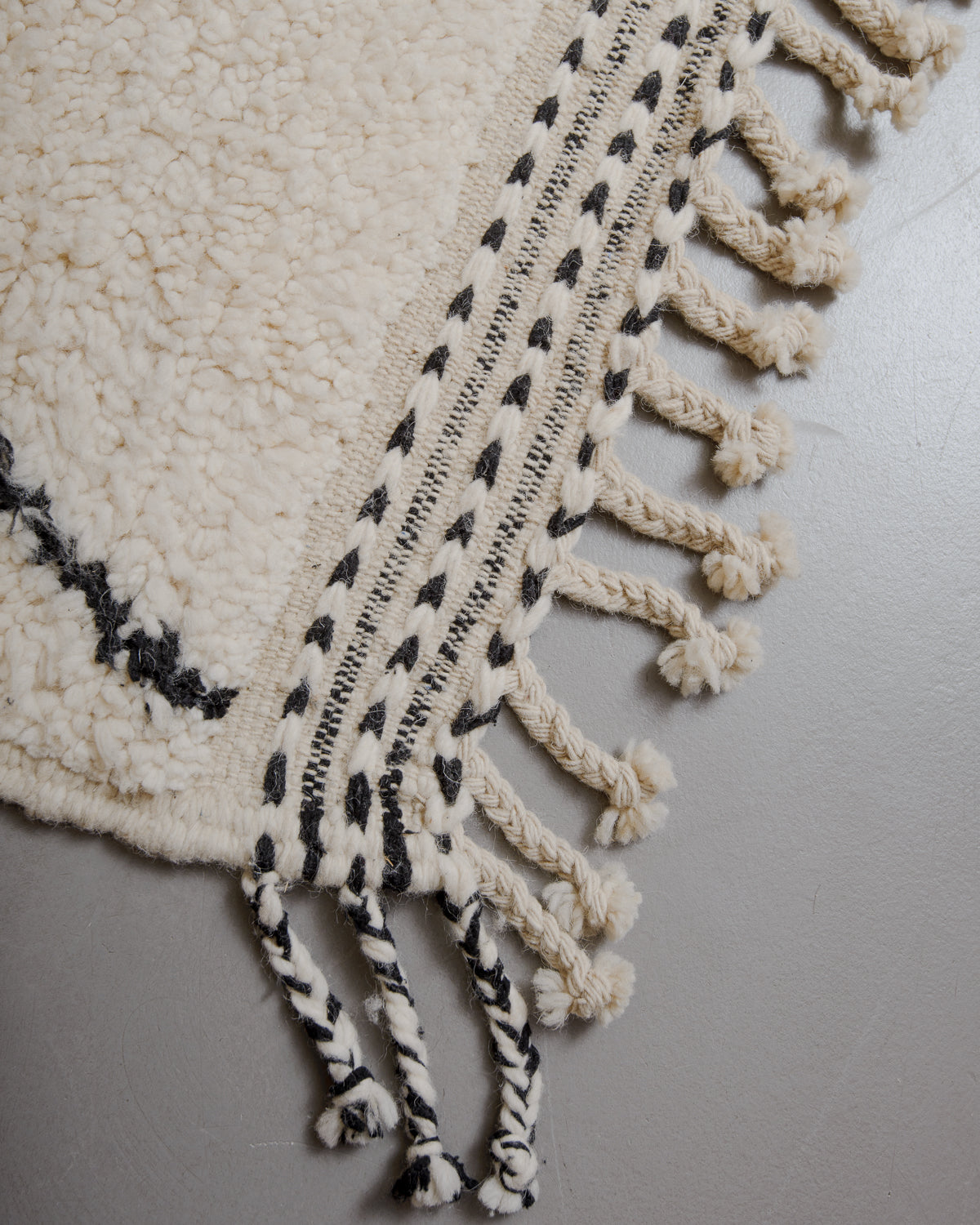 Edge of cream beniourain rug with natural wool tassels and black and white pattern along the edge.