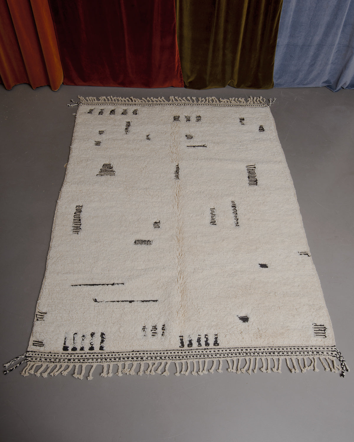 Berberlin Beniourain rug on grey floor in front of velvet curtains.