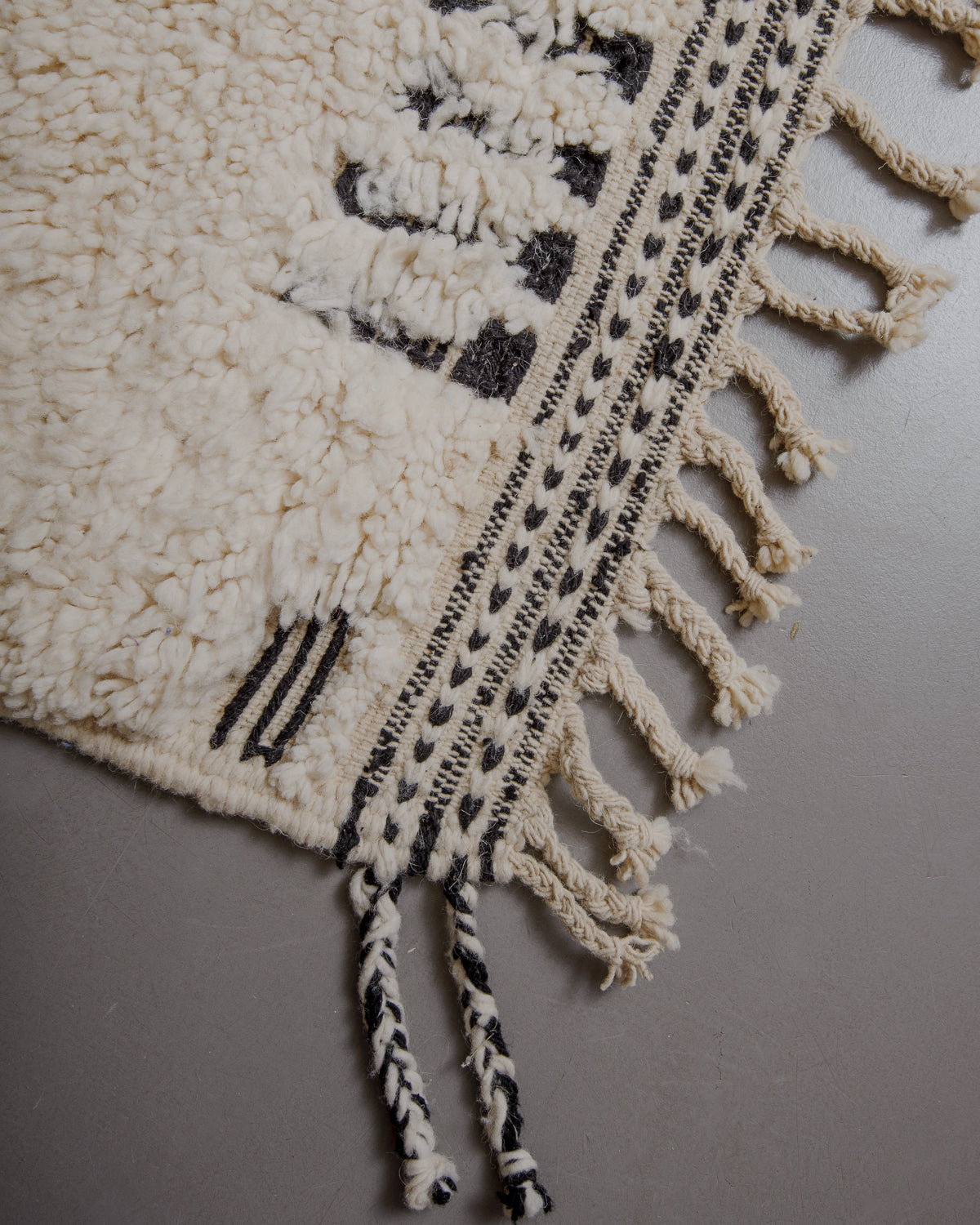 Edge of cream beniourain rug with natural wool tassels and black and white pattern along the edge.