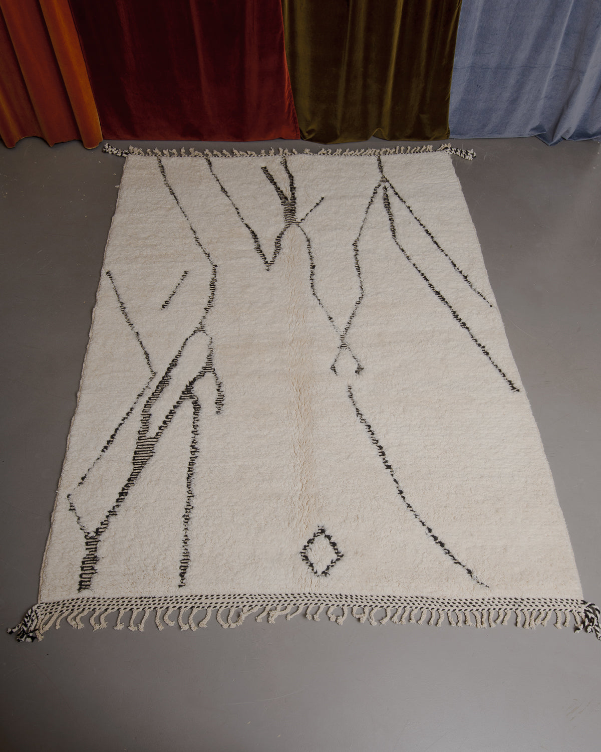Berberlin Beniourain rug on grey floor in front of velvet curtains.
