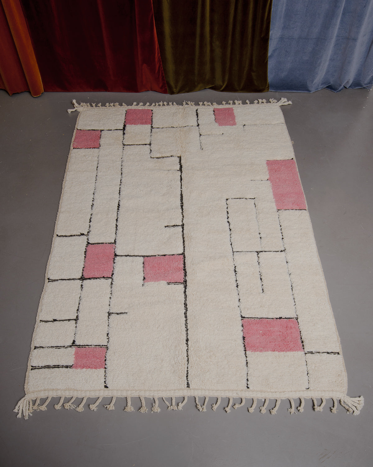 Berberlin Beniourain rug on grey floor in front of velvet curtains.