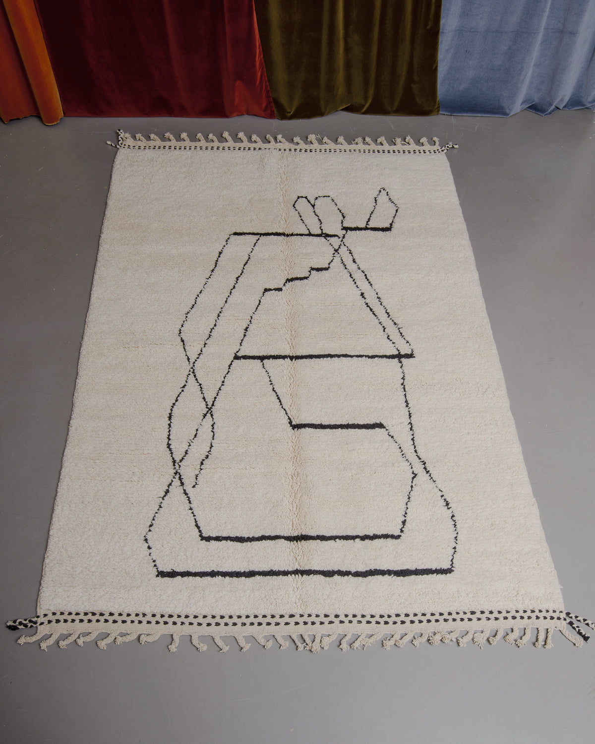 Berberlin Beniourain rug on grey floor in front of velvet curtains.