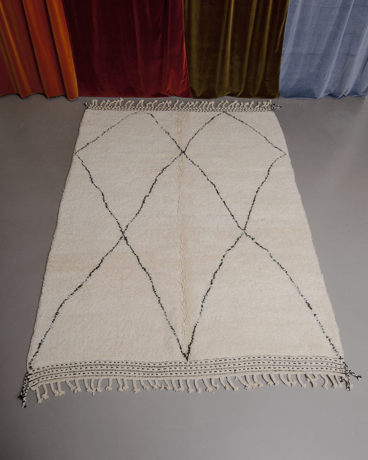 Berberlin Beniourain rug on grey floor in front of velvet curtains.