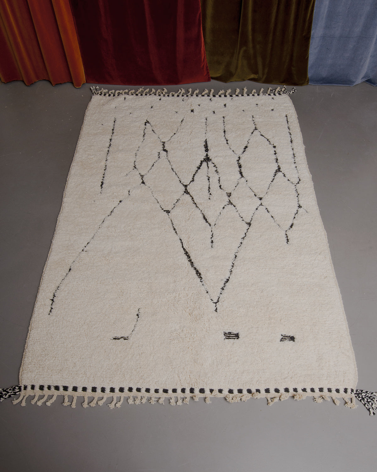 Berberlin Beniourain rug on grey floor in front of velvet curtains.