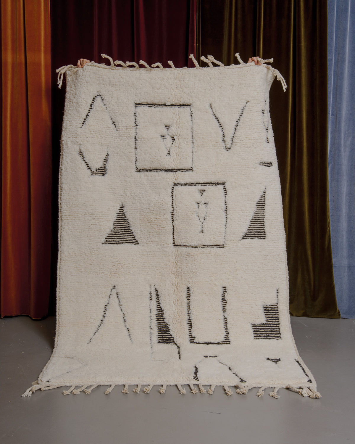 Cream and black Berberlin Beniourain rug held up in front of velvet curtains.