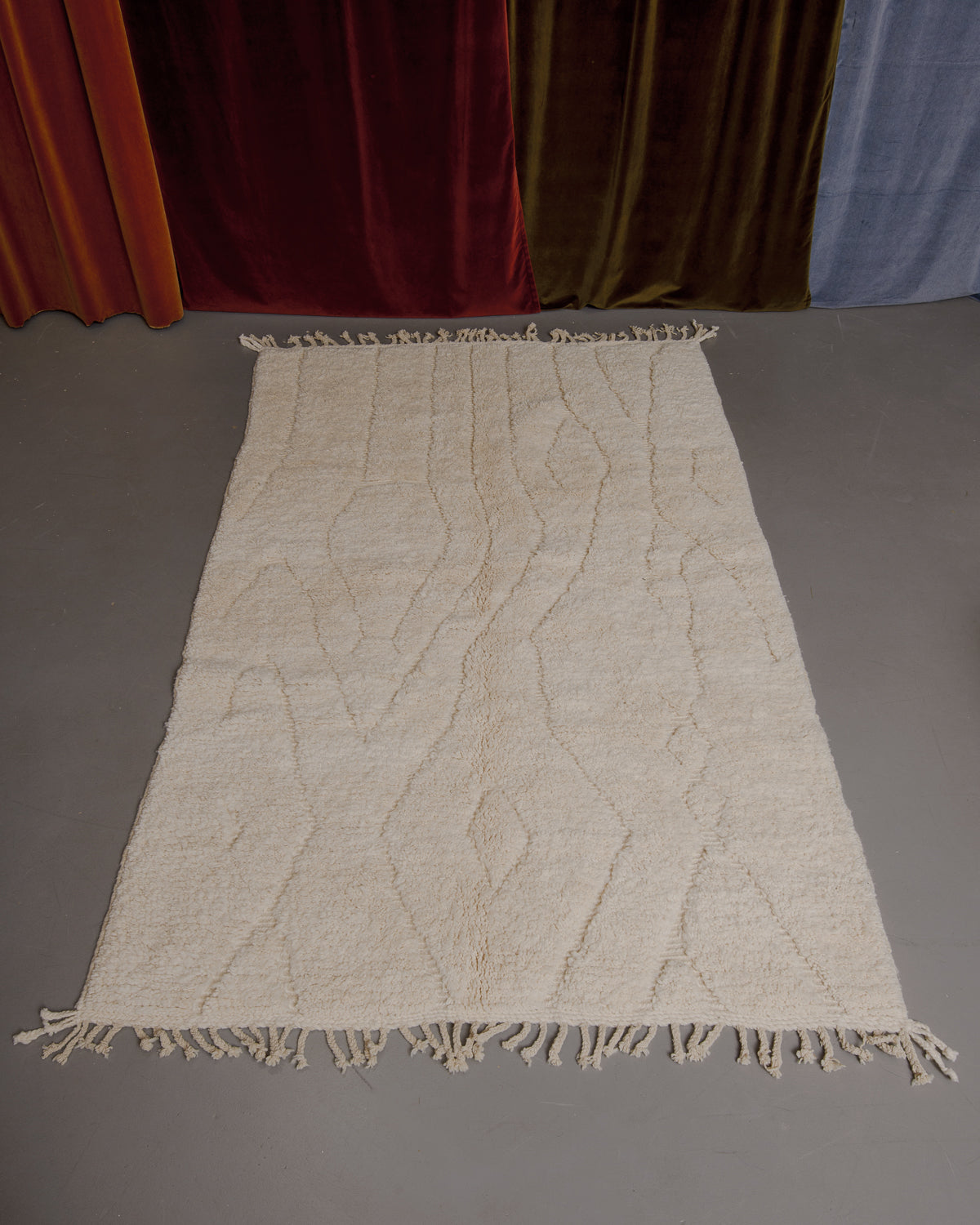 Berberlin Beniourain rug on grey floor in front of velvet curtains.