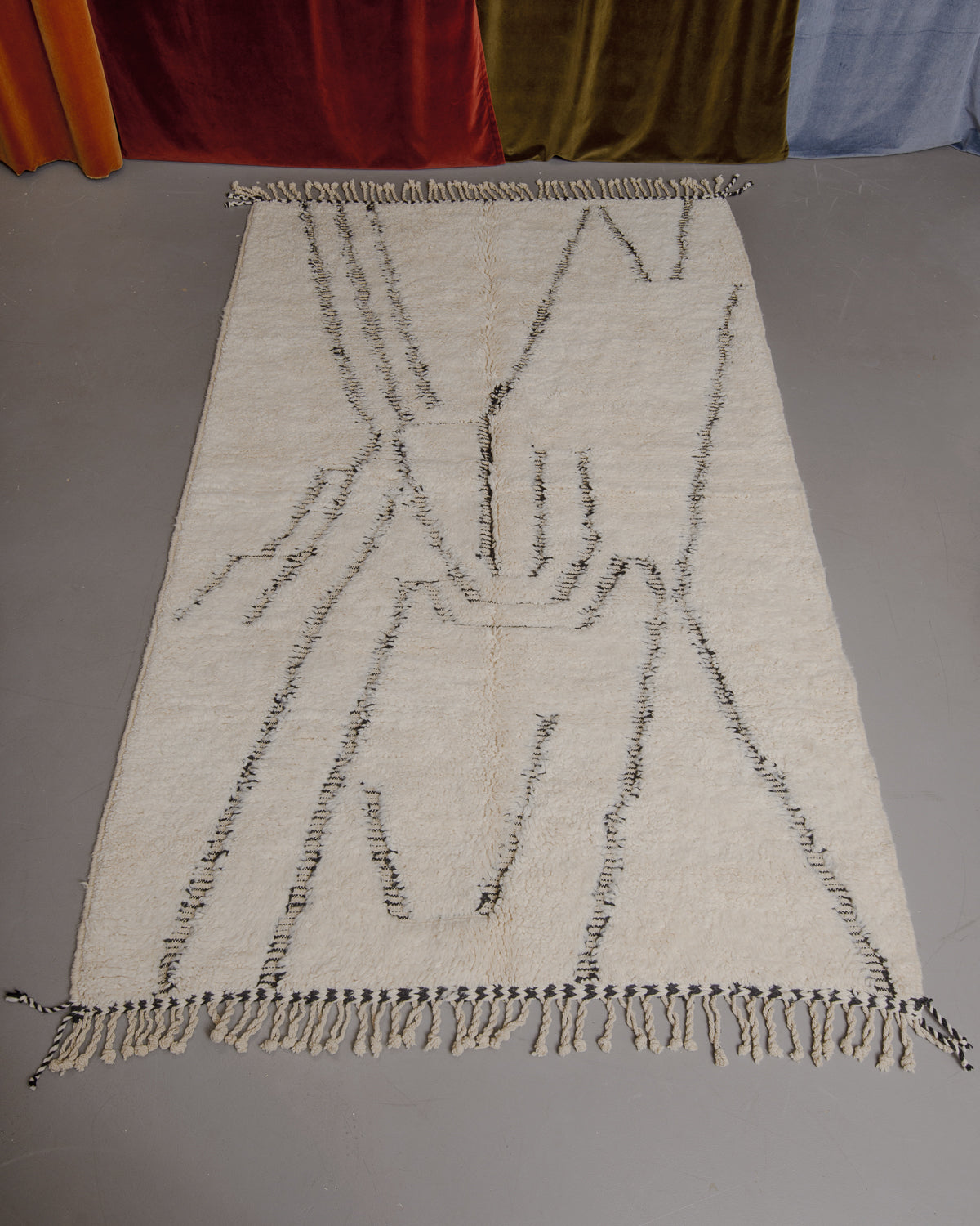 Berberlin Beniourain rug on grey floor in front of velvet curtains.