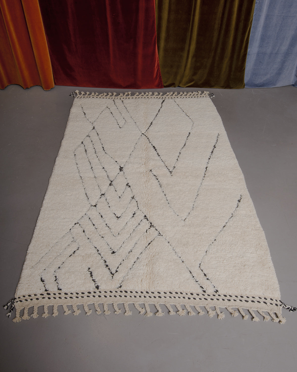 Berberlin Beniourain rug on grey floor in front of velvet curtains.