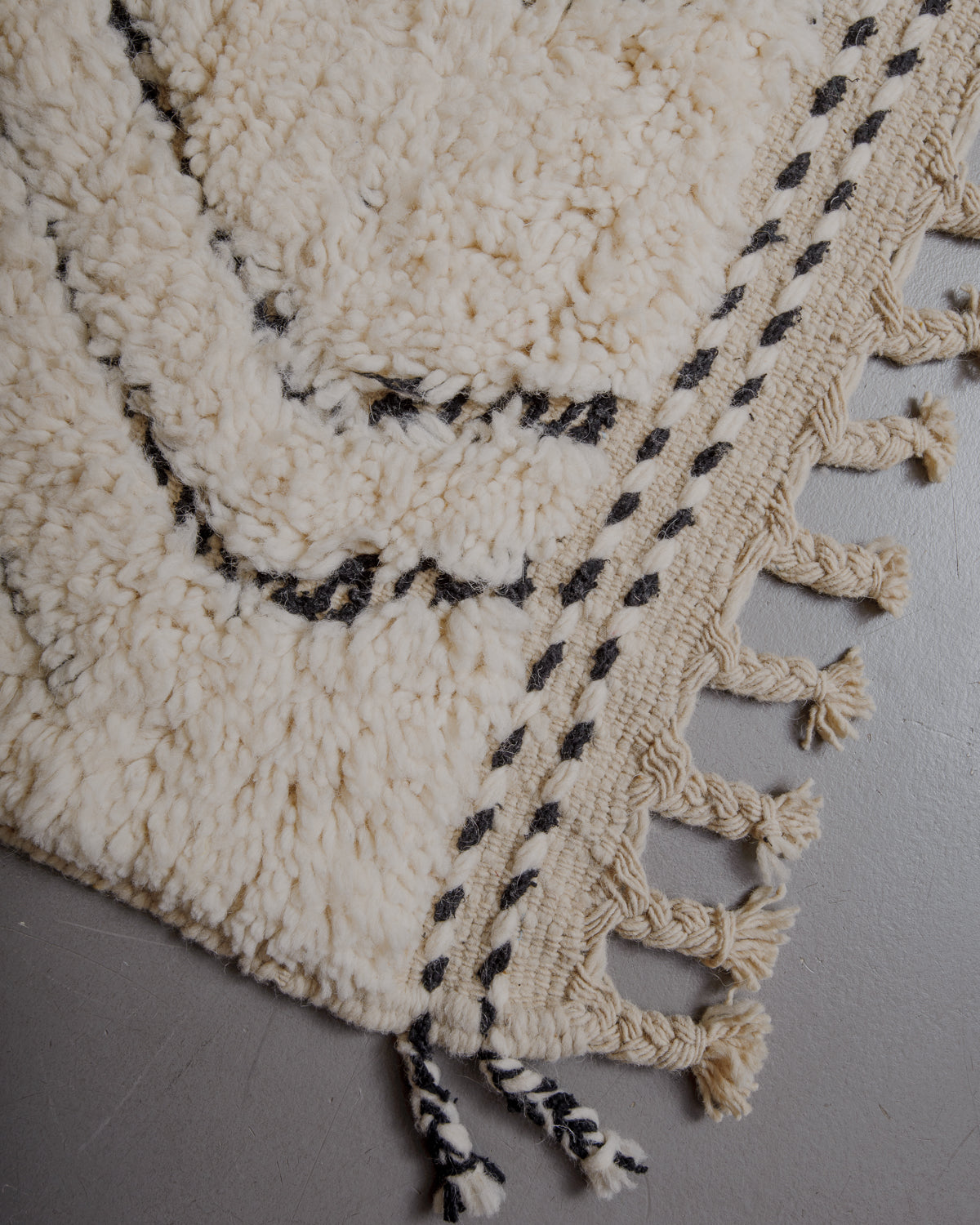 Edge of cream beniourain rug with natural wool tassels and black and white pattern along the edge.