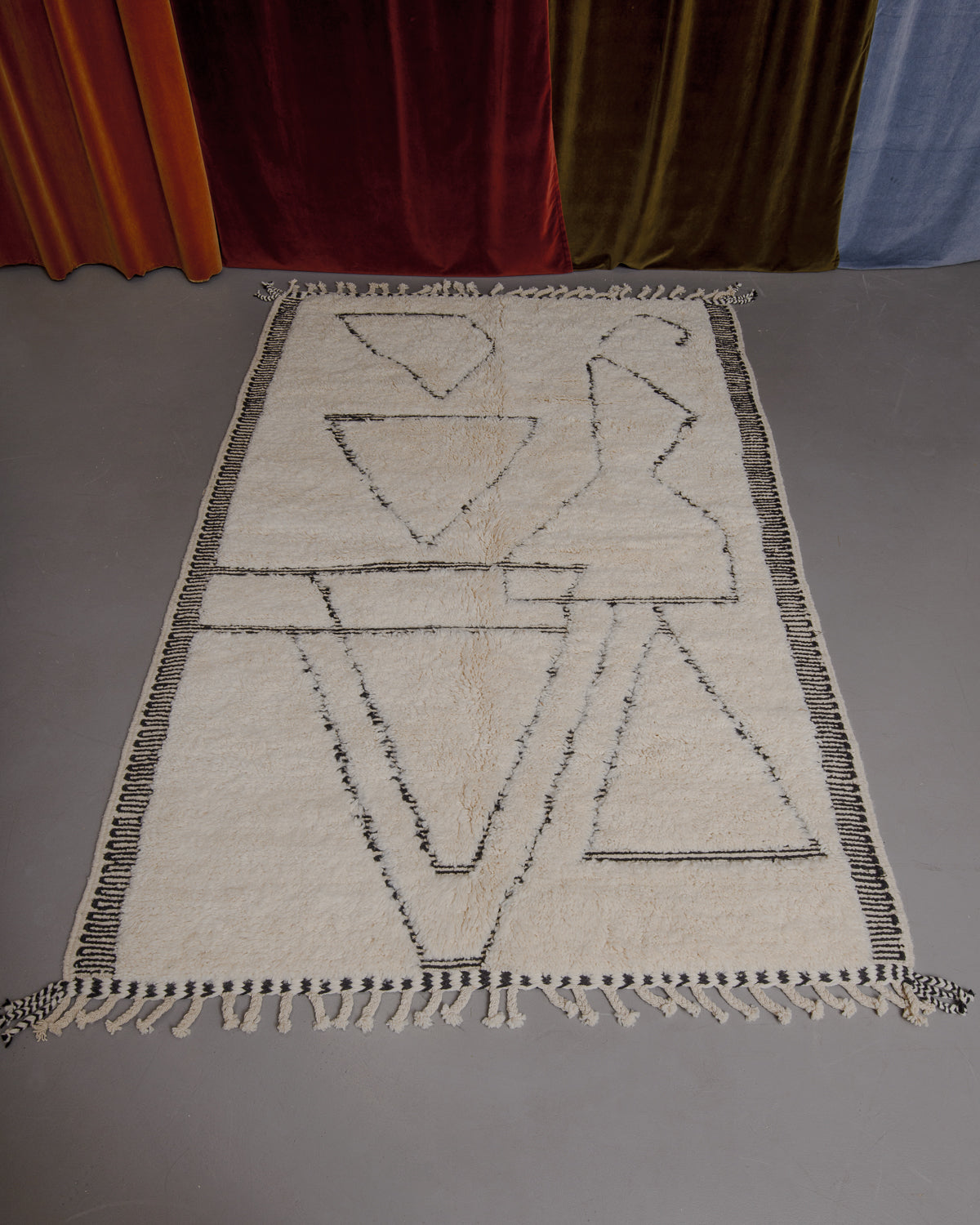 Berberlin Beniourain rug on grey floor in front of velvet curtains.