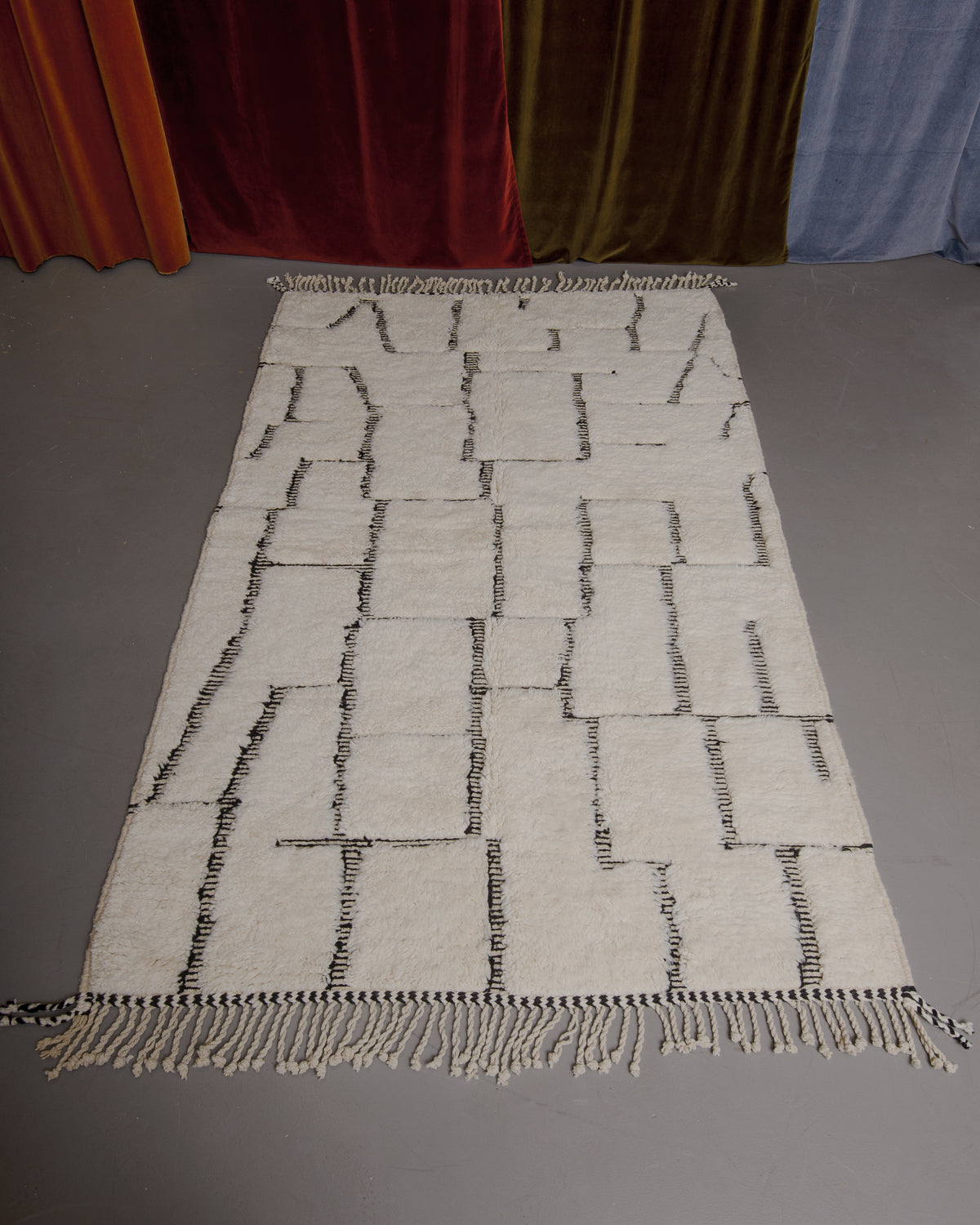 Berberlin Beniourain rug on grey floor in front of velvet curtains.
