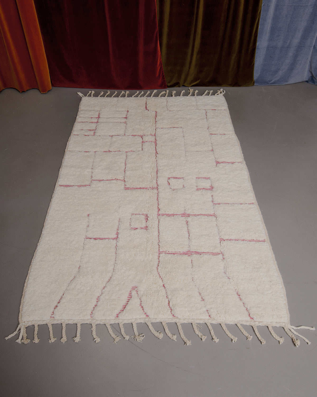 Berberlin Beniourain rug on grey floor in front of velvet curtains.