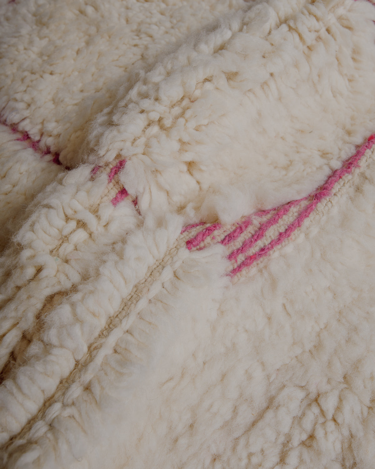 Fluffy cream wool pile with pink embroidery.