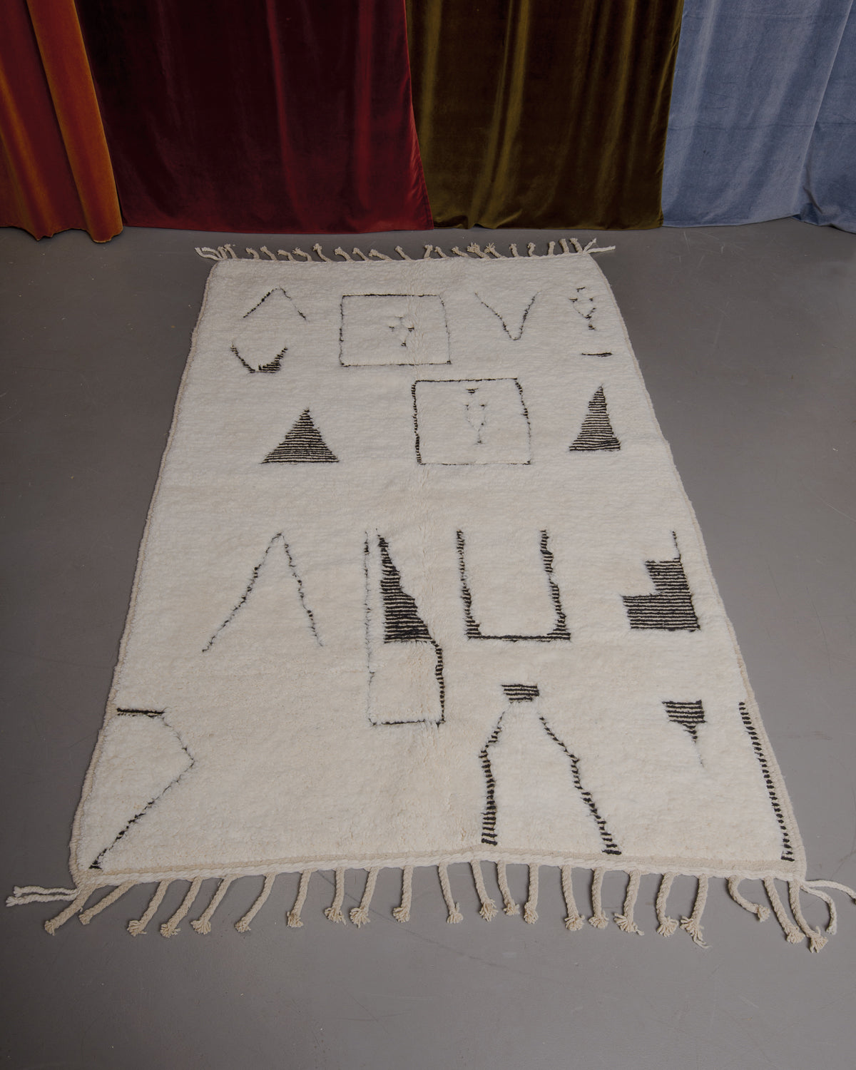 Berberlin Beniourain rug on grey floor in front of velvet curtains.
