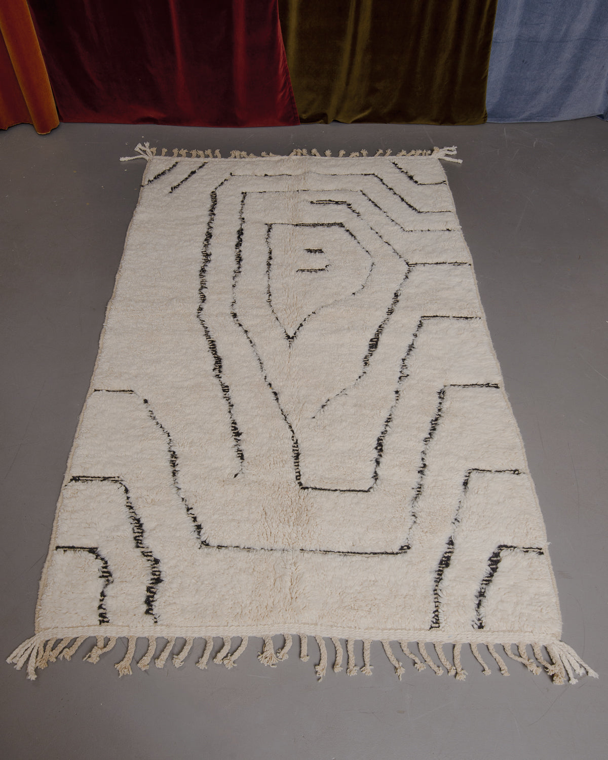Berberlin Beniourain rug on grey floor in front of velvet curtains.