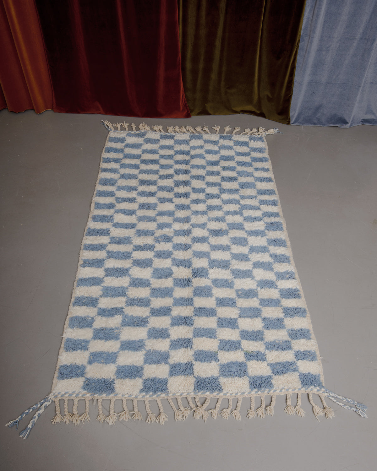 Berberlin Beniourain rug on grey floor in front of velvet curtains.