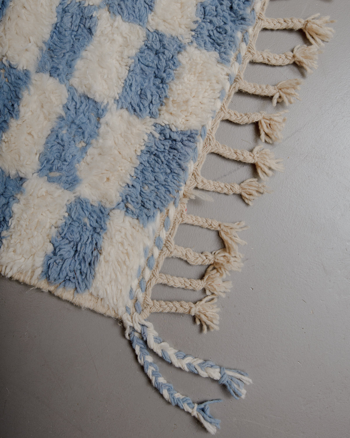 Corner of cream and blue checkered beniourain rug with natural wool tassels.