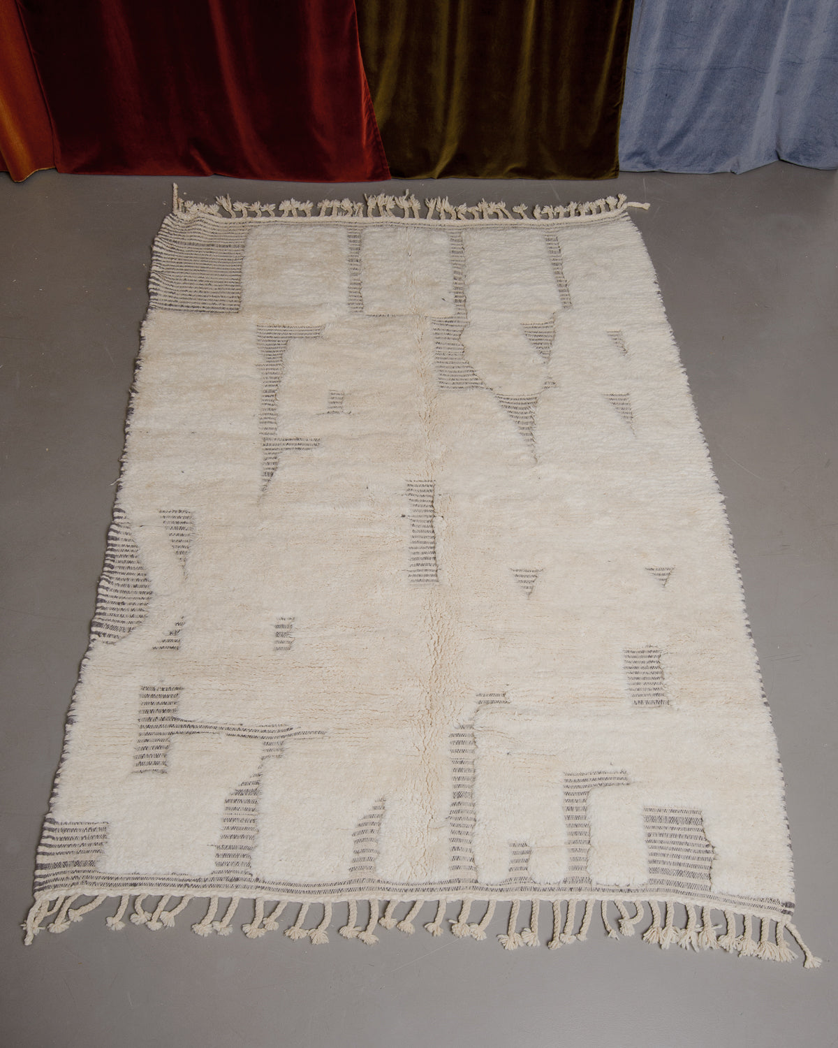 Cream and grey Berberlin Beniourain rug on grey floor in front of velvet curtains.
