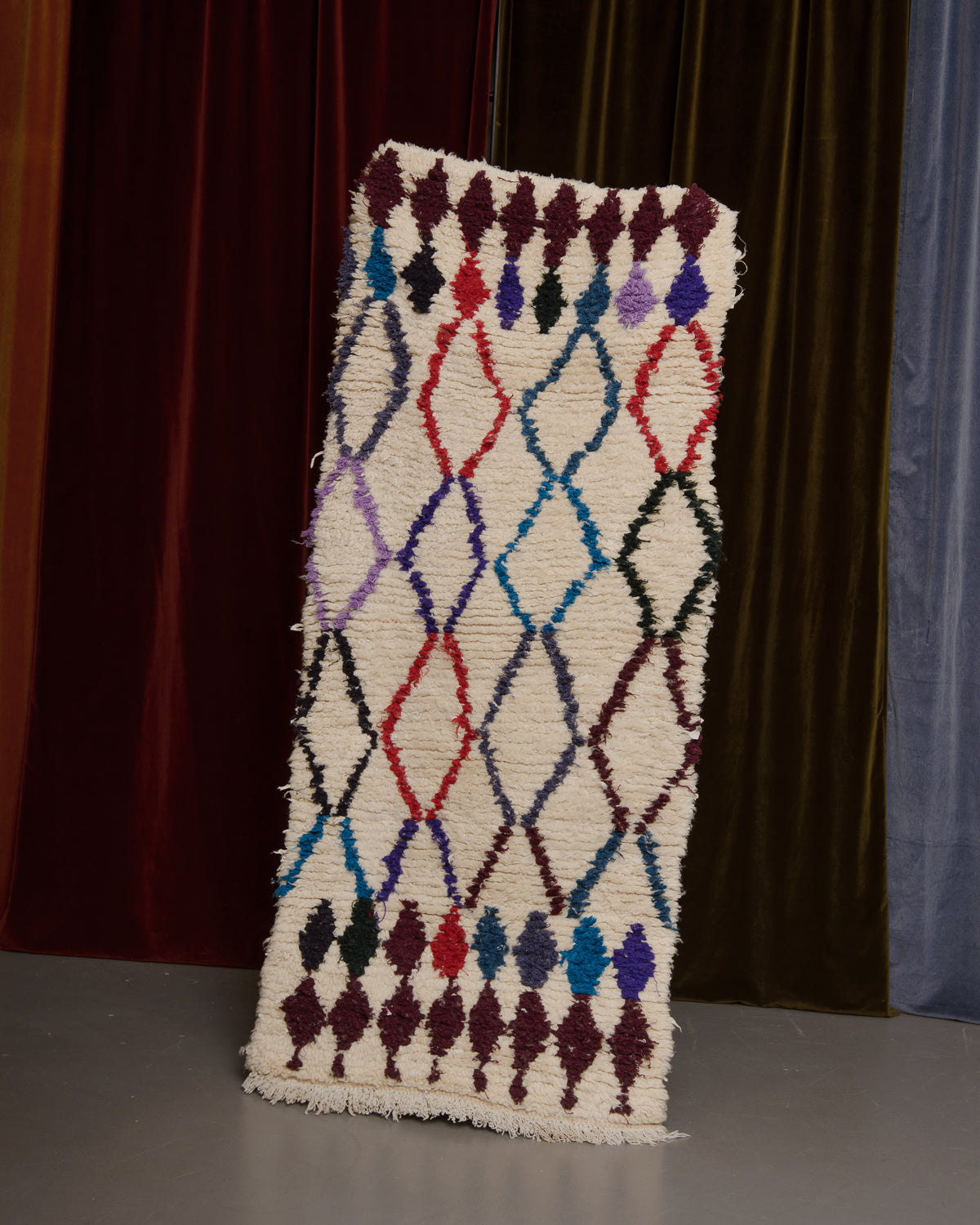 Vintage Berberlin wool runner rug being held up in front of velvet curtains.
