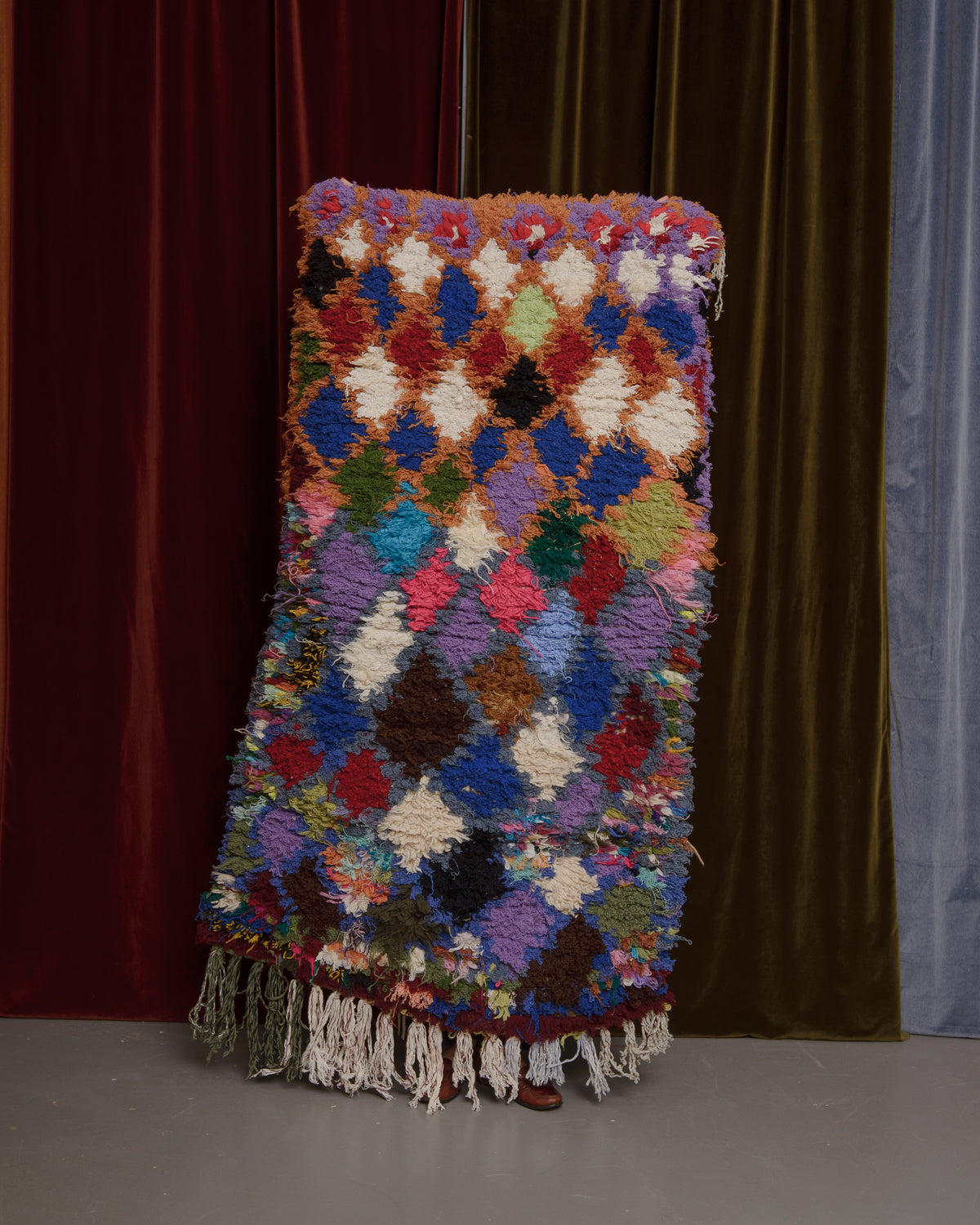 Vintage Berberlin wool runner rug being held up in front of velvet curtains.