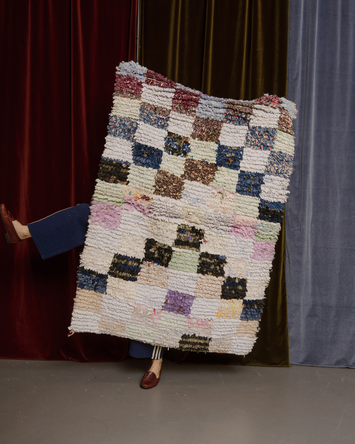 Vintage Berberlin boucherouite runner rug being held up in front of velvet curtains with a leg kicked out to the side from behind.
