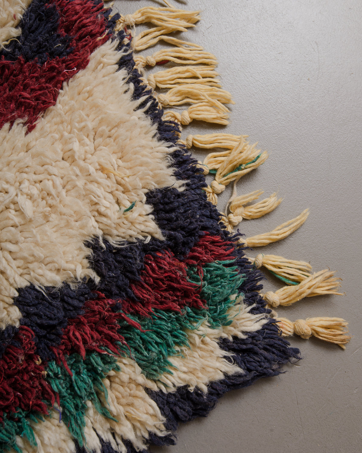 Close up of vintage  wool rug with a shaggy texture and cream tassels.