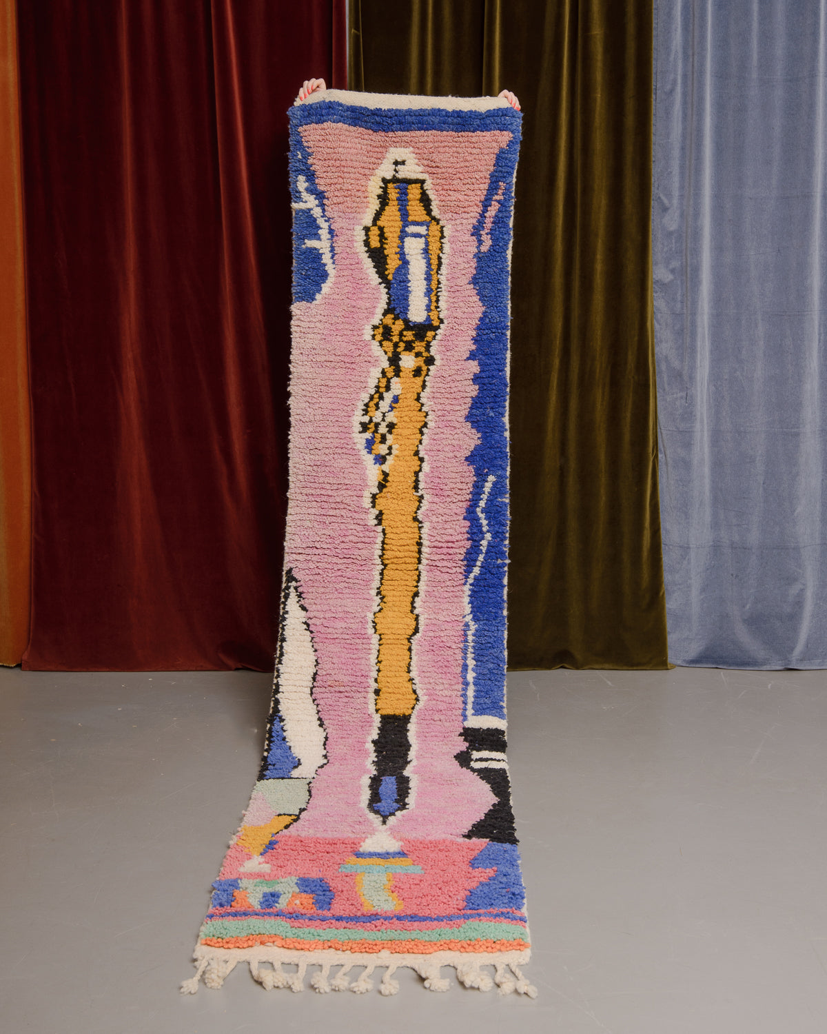 Vintage Berberlin boujaad runner rug being held up in front of a velvet curtains.