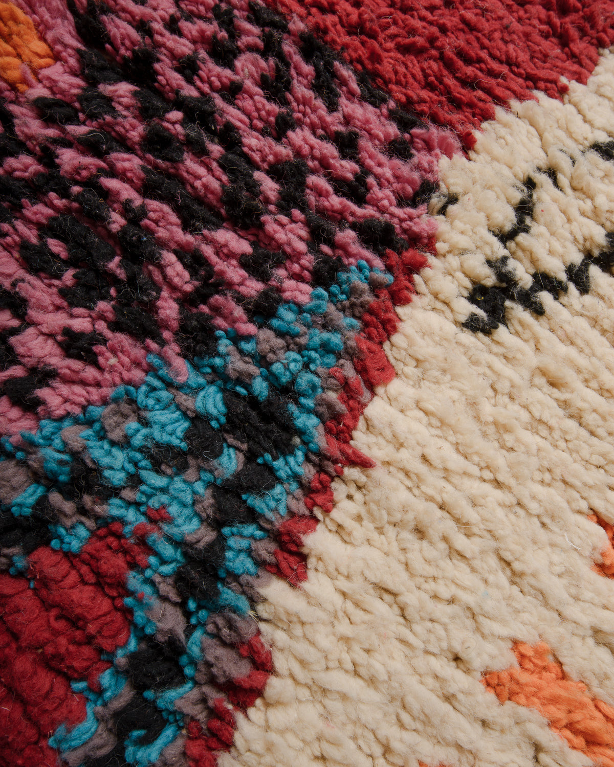 Surface of Boujaad rug with blue, black, pink, red, orange and cream wool.