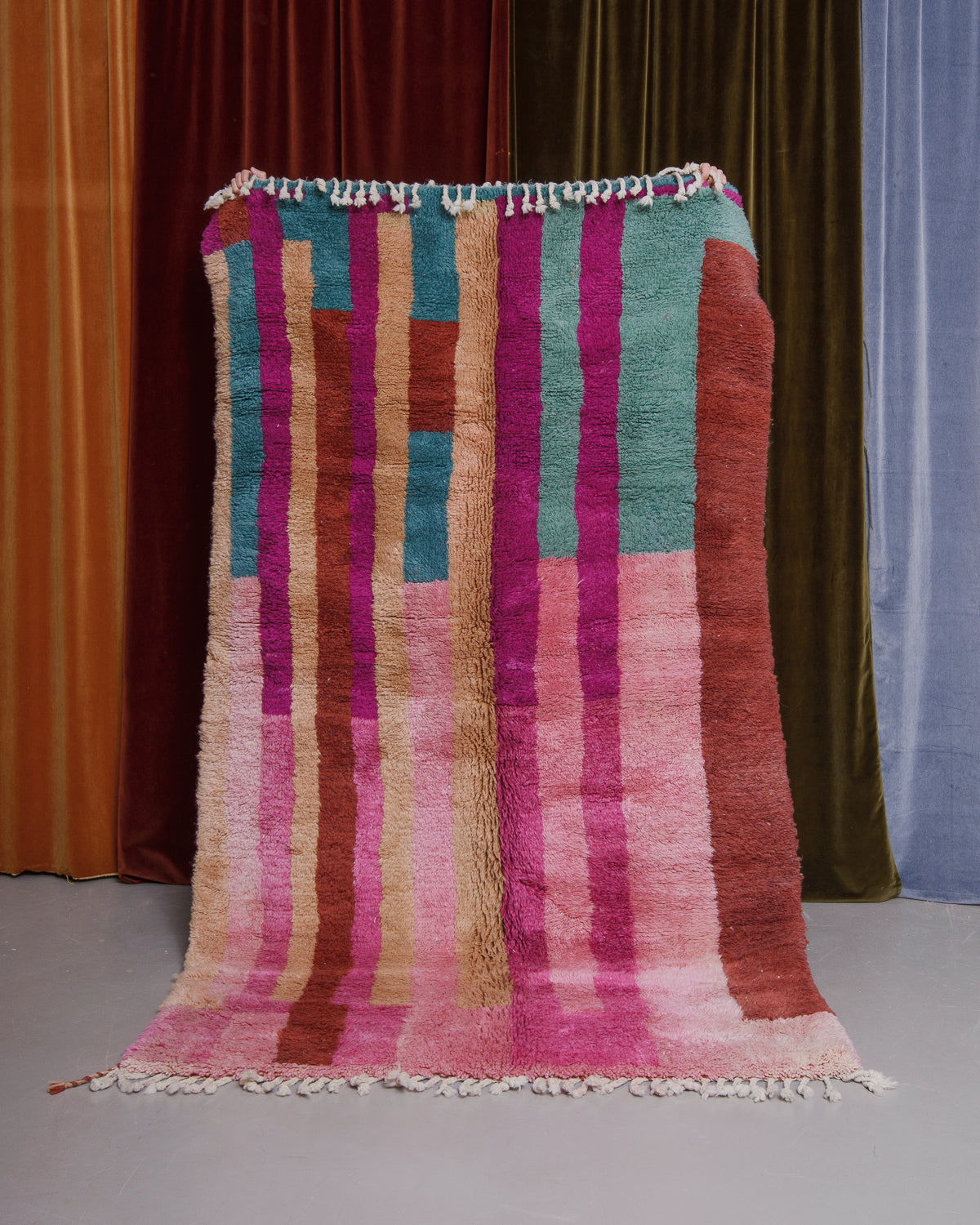 Berberlin Finest beniourain rug held in front of velvet curtains. 