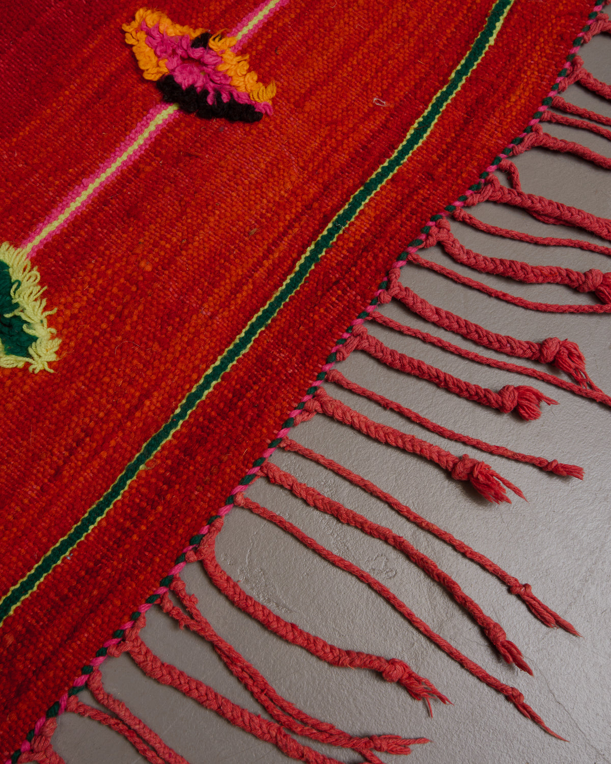 Edge of red kelim rug with red tassels in different lengths and thicknesses.