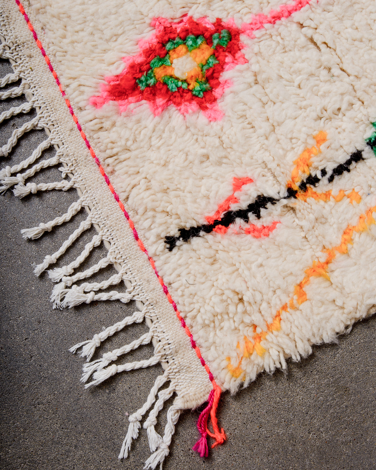 Corner of cream Azilal rug with white cotton tassels across the end and pink and orange tassels at the corner.  