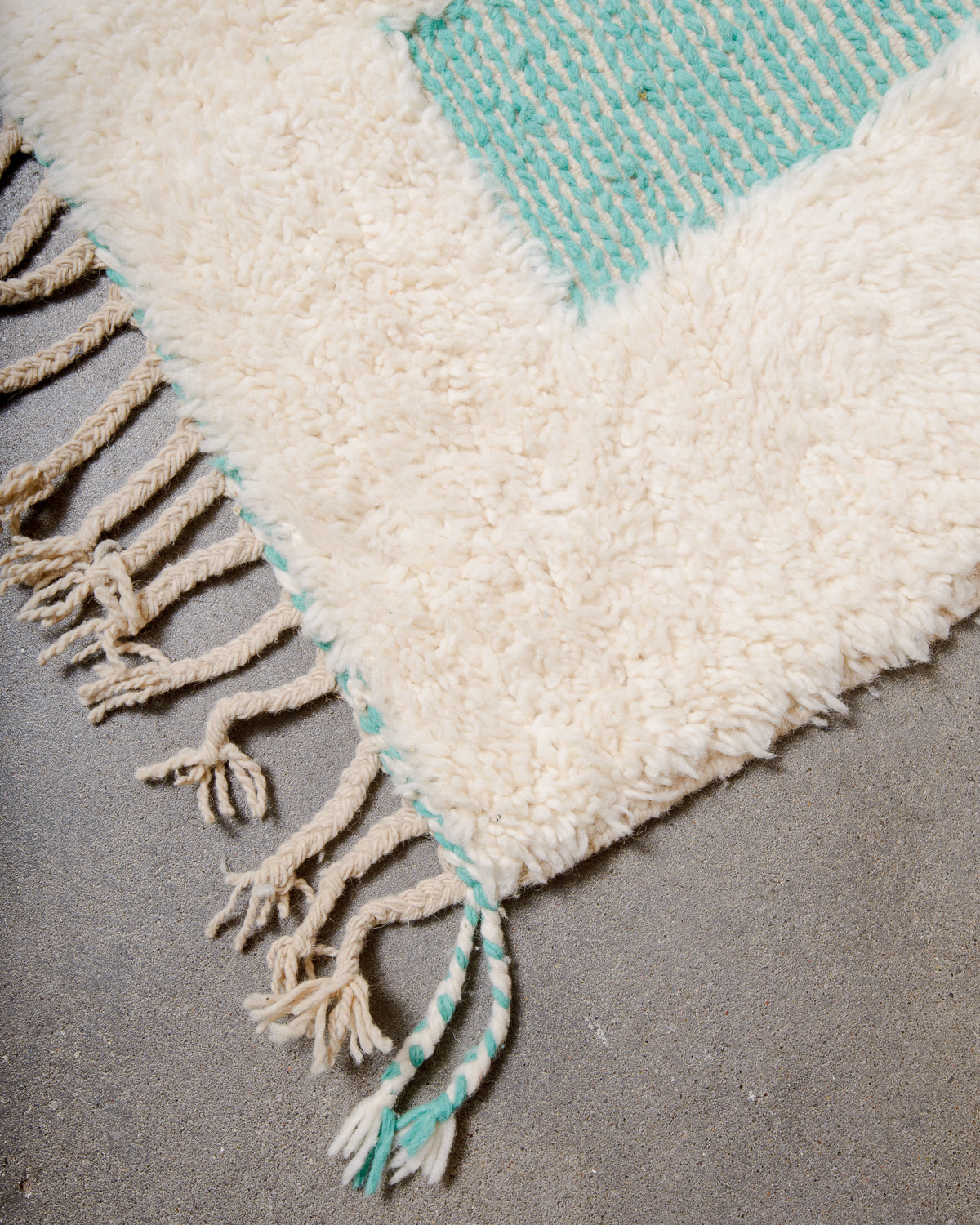 Corner of Berber rug with cream and turquoise wool and natural wool tassels. 