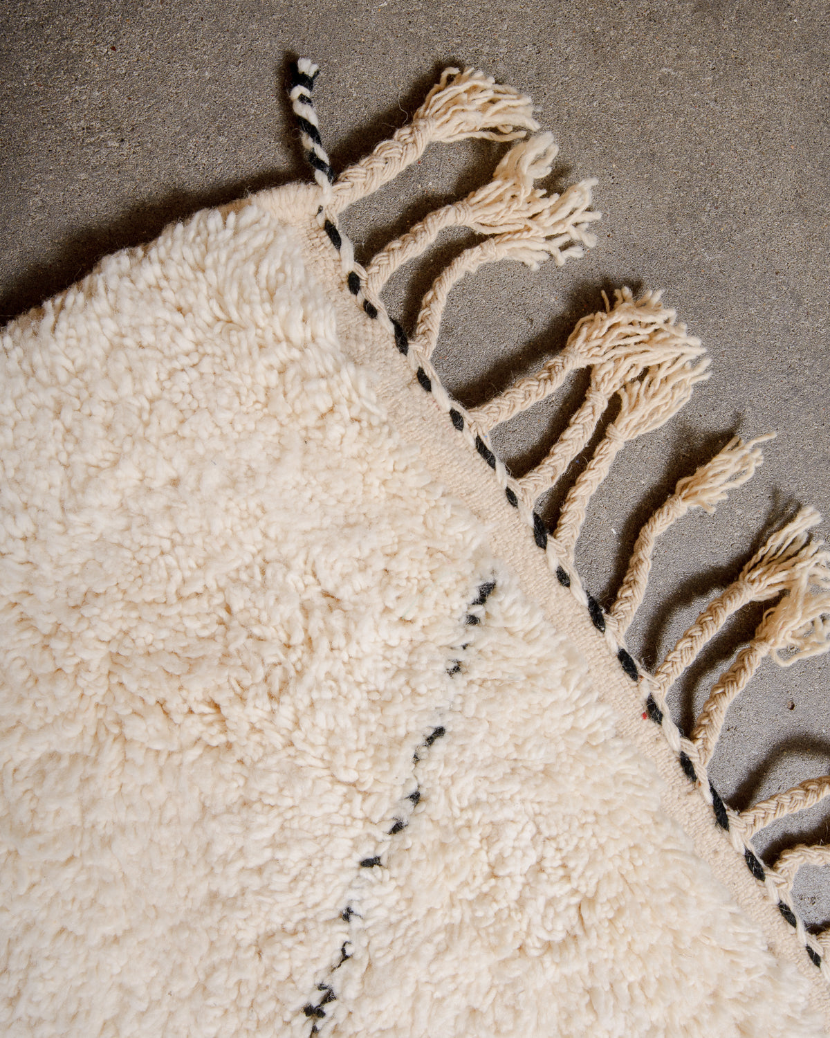 Natural wool tassels on edge of Berber rug with black and white details.