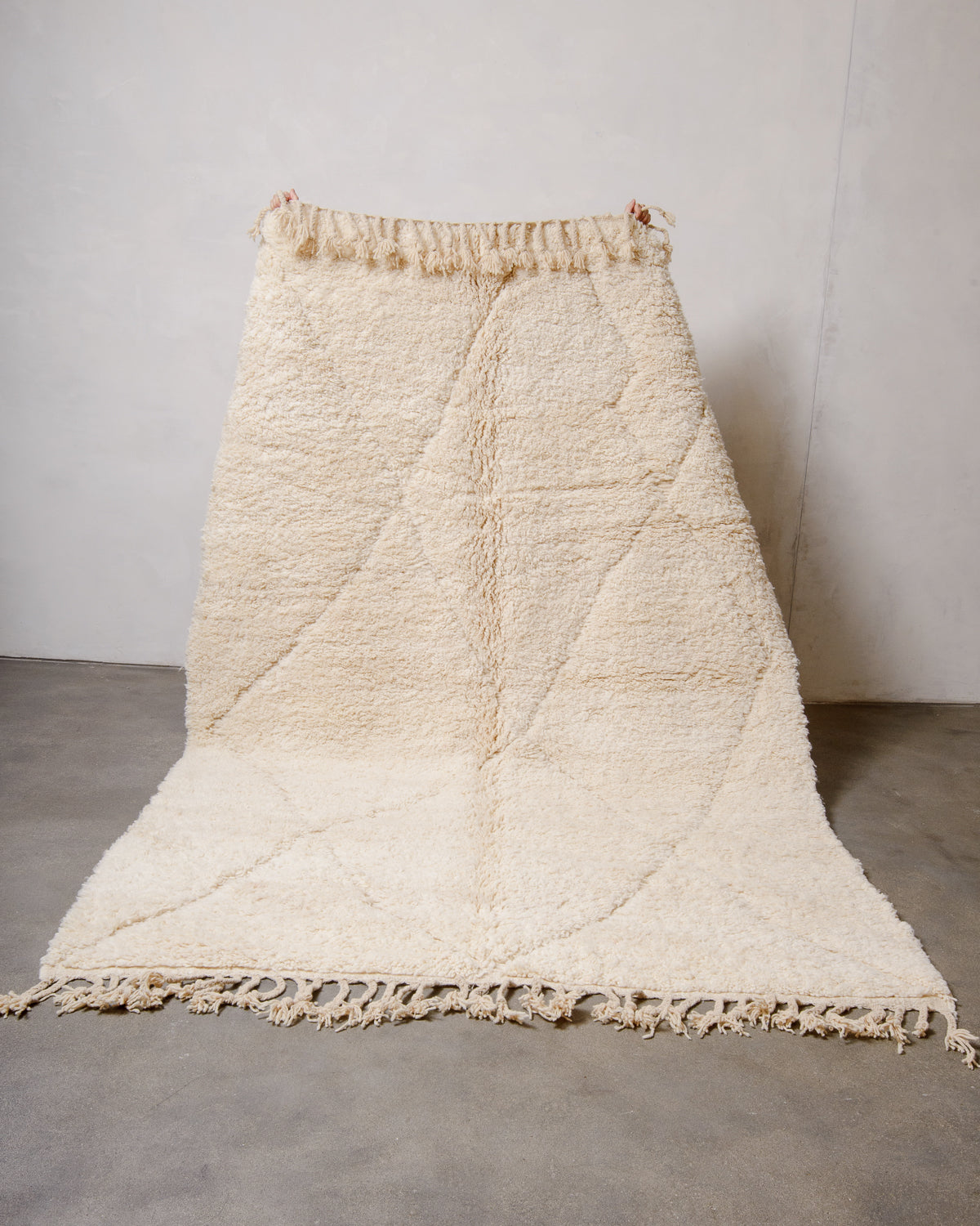 Berberlin Beniourain rug being held up in front of a white wall. 