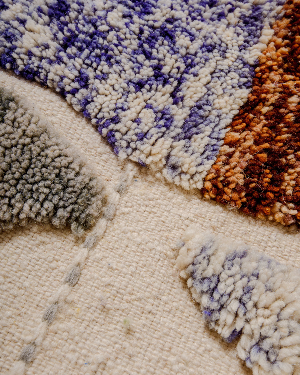 Detail of wool Berber rug with cream flat woven area and raised knotted sections in grey, blue and brown wool. 