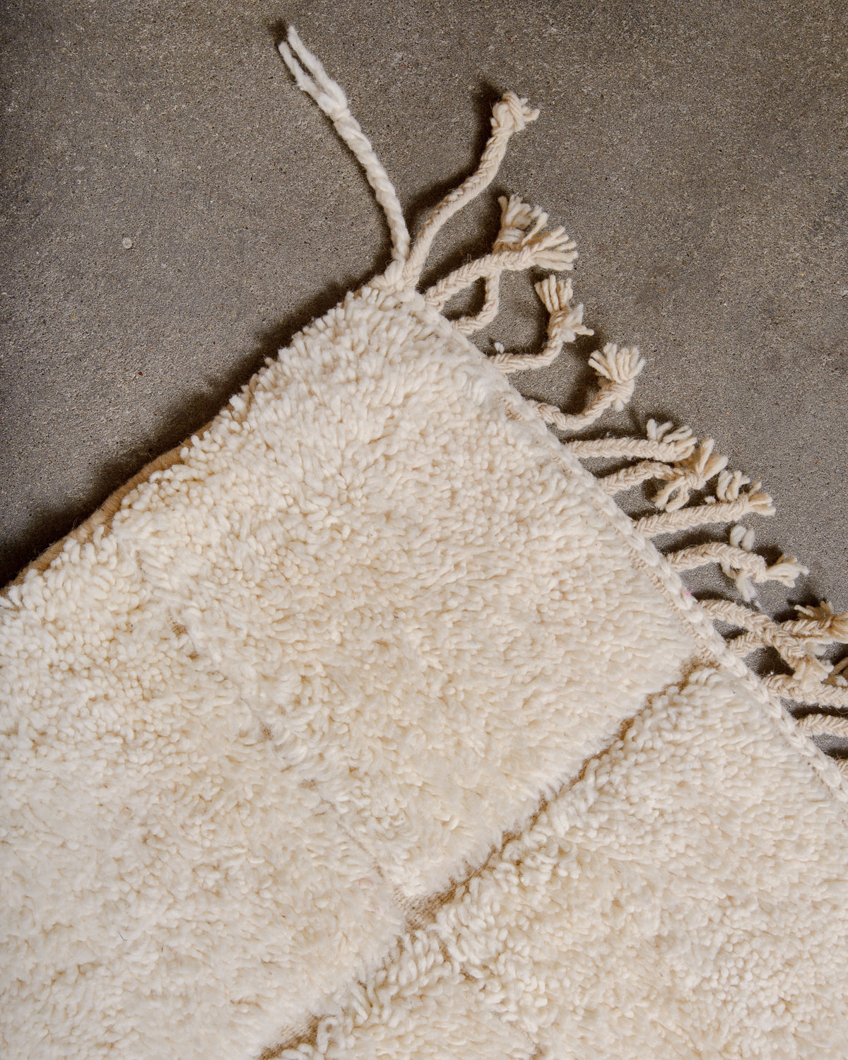 Corner of Berberlin Beniourain rug made of cream wool with natural wool tassels.