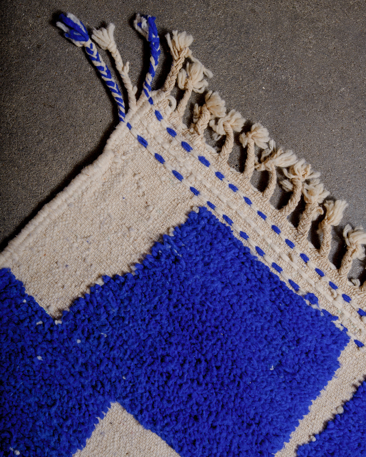 Corner of "Maram" Special Edition Beniourain rug with natural wool tassels at the end with two blue and cream tassels at the corner.