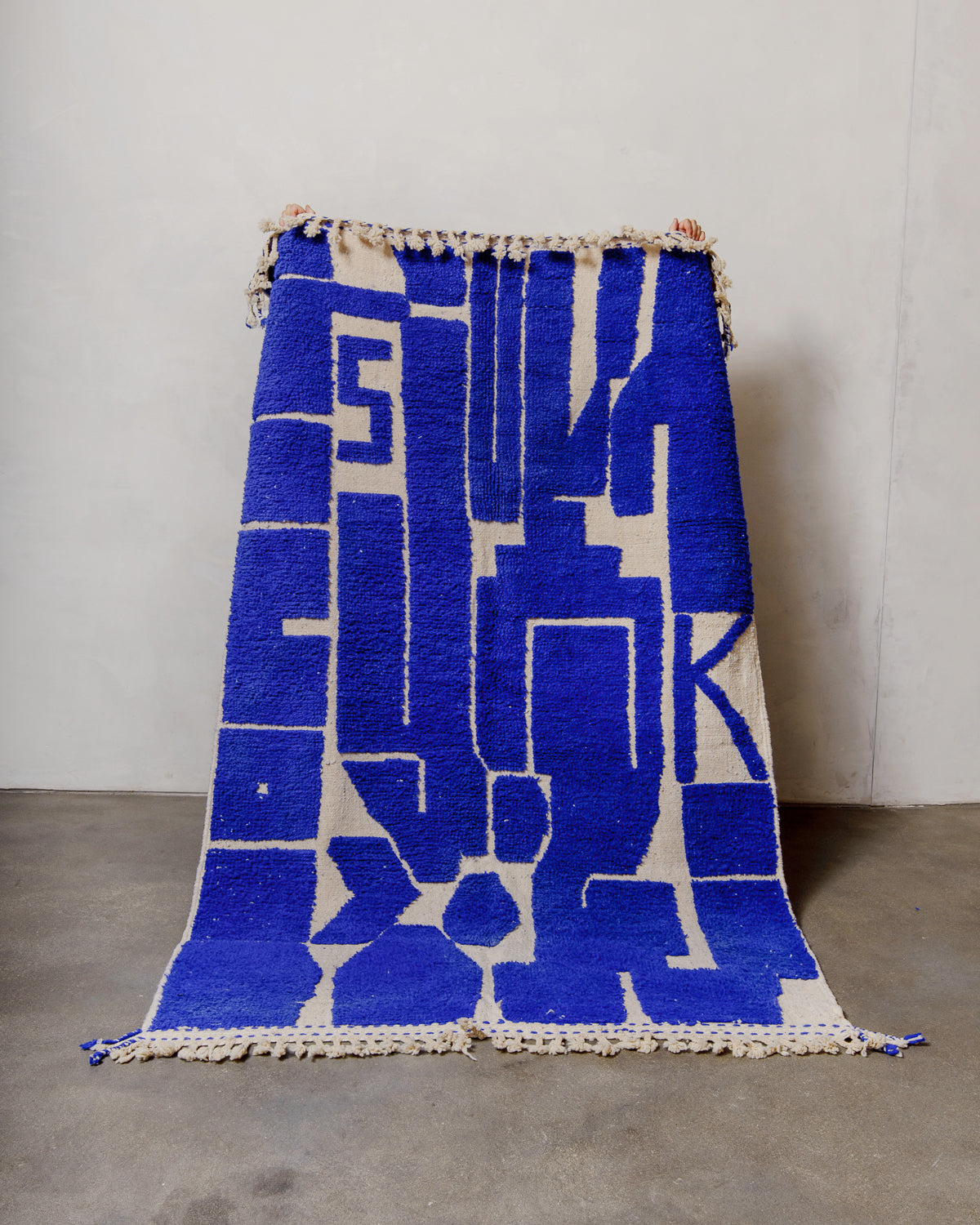 Berberlin Beniourain rug in cobalt blue and cream, being held up in front of a white wall. 